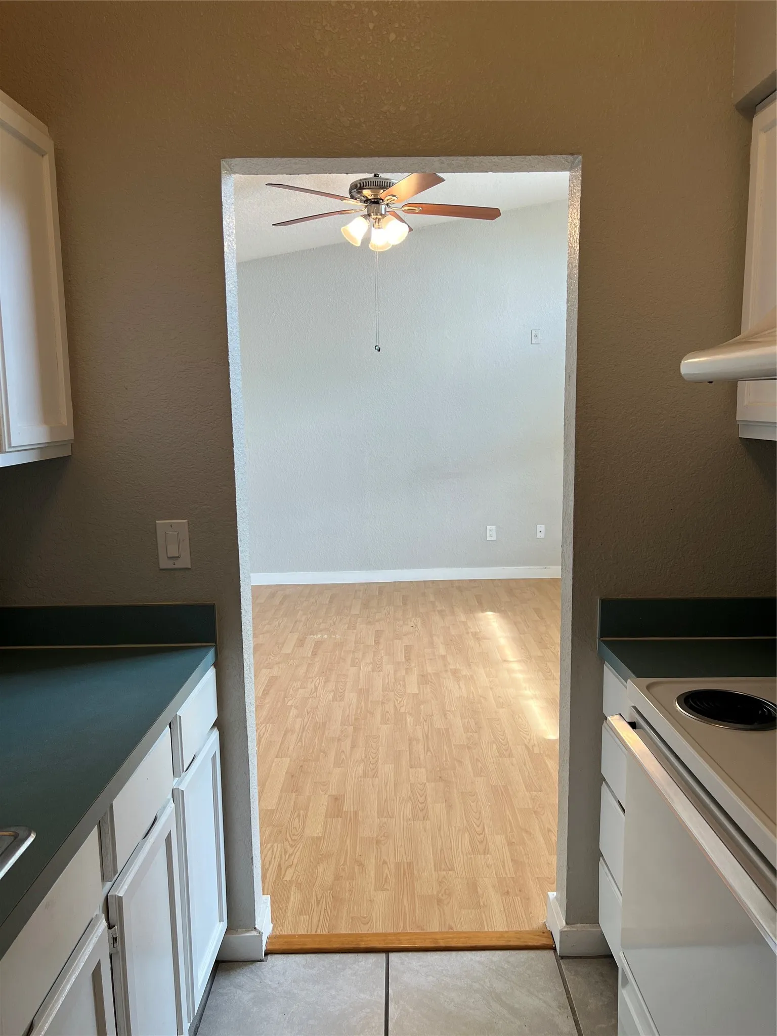 White cabinetry with contrasting countertops, tile flooring, wood-finish flooring, and a ceiling fan with integrated lighting