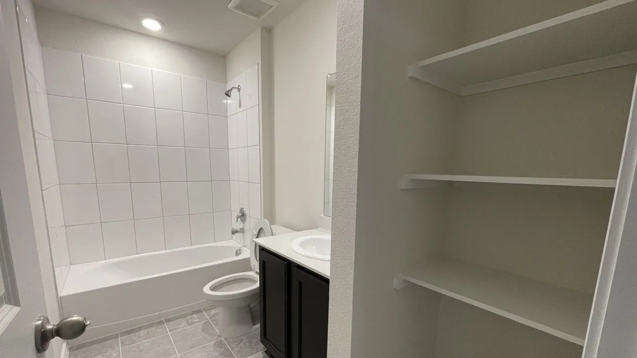 Bathroom featuring a tub/shower combination with white subway tile surround, dark wood-finish vanity with a white countertop and integrated sink, and grey tile flooring
