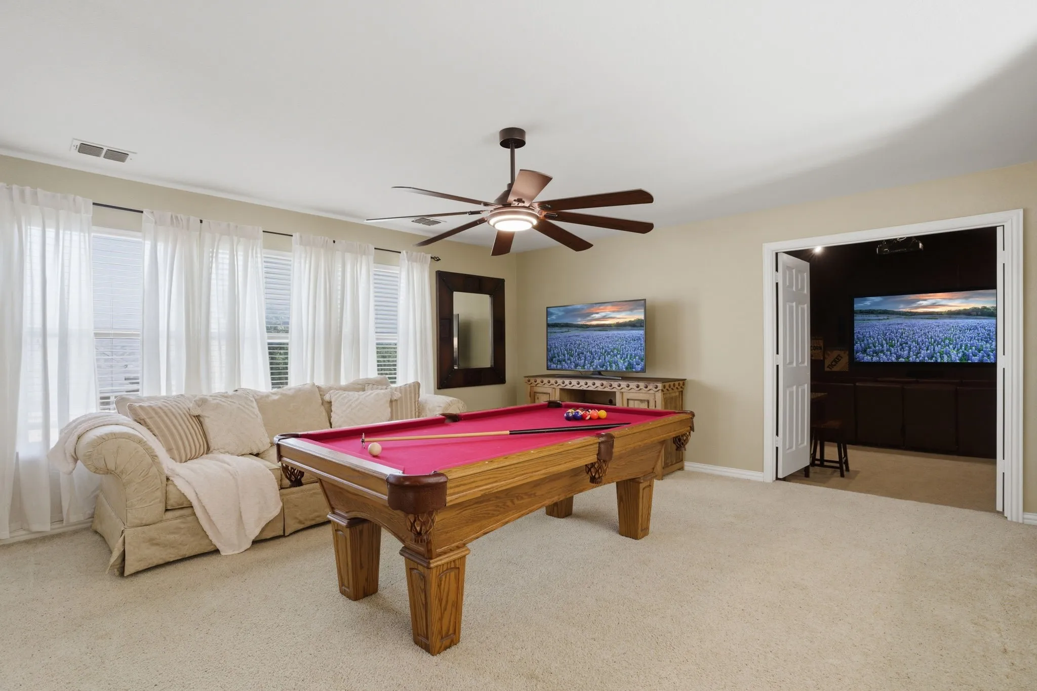 The second-floor game room features plush carpeting and three large windows that fill the space with natural light, creating a bright and airy atmosphere. A new ceiling fan adds comfort, while a closet accessed through French doors includes custom shelving ideal for games, books, and toys.
