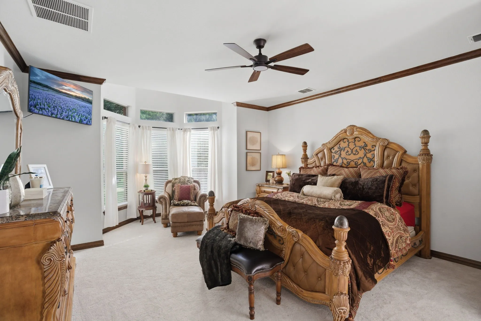 The luxurious primary suite features plush brand new carpeting, a bay window creating a cozy sitting area with backyard views, crown molding, and a ceiling fan.