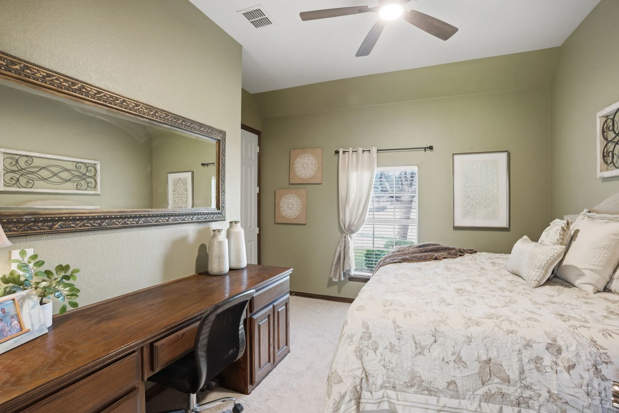 Bedroom 2, located on the first floor, features plush new carpeting, a built-in desk with cabinetry and drawers ideal for work or study, and a walk-in closet for ample storage. A ceiling fan adds comfort, while a window overlooking the front yard fills the space with natural light.
