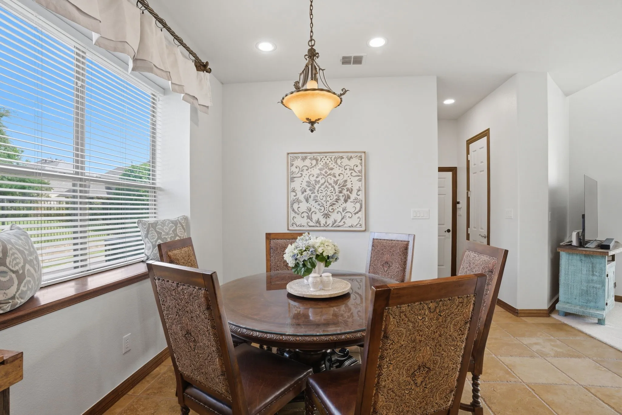 The spacious breakfast room off the kitchen includes travertine floors for easy clean up, a large window with plant ledge allowing in natural light, and a chic light fixture that centers the space.
