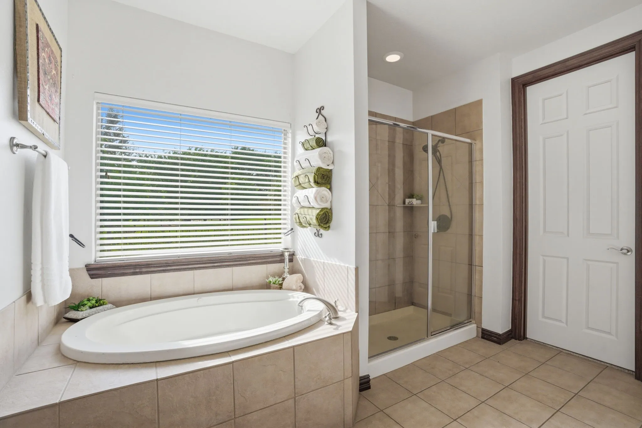 A cozy corner showcases a Lasco Luxury Bathware jetted soaking tub beneath a window, creating a spa-like retreat. The separate shower includes a tile surround, built-in shampoo shelf, and a Pfister designer system with shower head and body sprays.