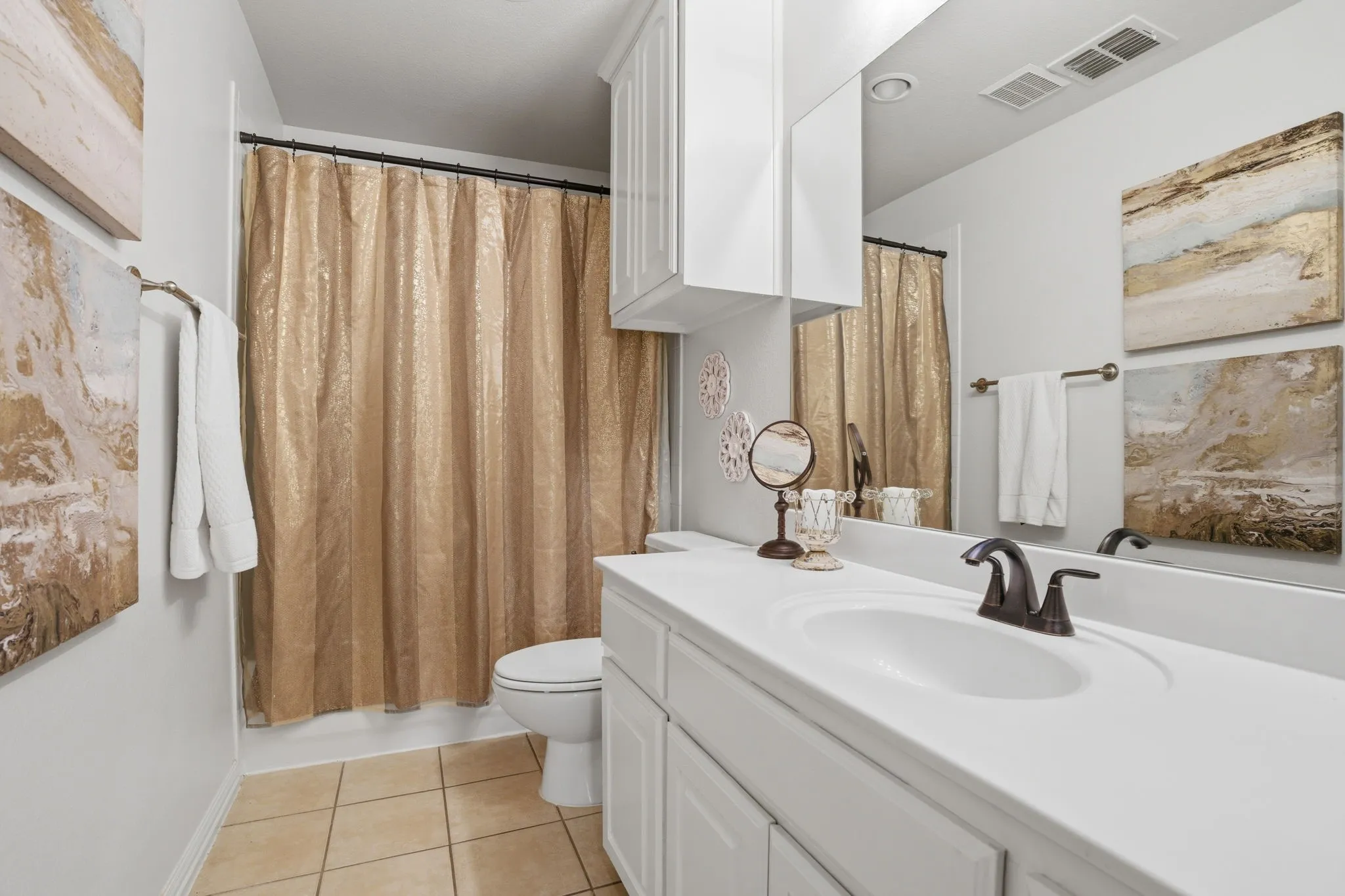 Bathroom 3, conveniently located adjacent to Bedroom 3, is a full bath featuring tile flooring and a built-in white vanity accented by brushed bronze fixtures. Upper cabinetry provides additional storage, while the tub and shower combination is finished with a crisp white tile surround and outfitted with a Pfister faucet and shower system.
