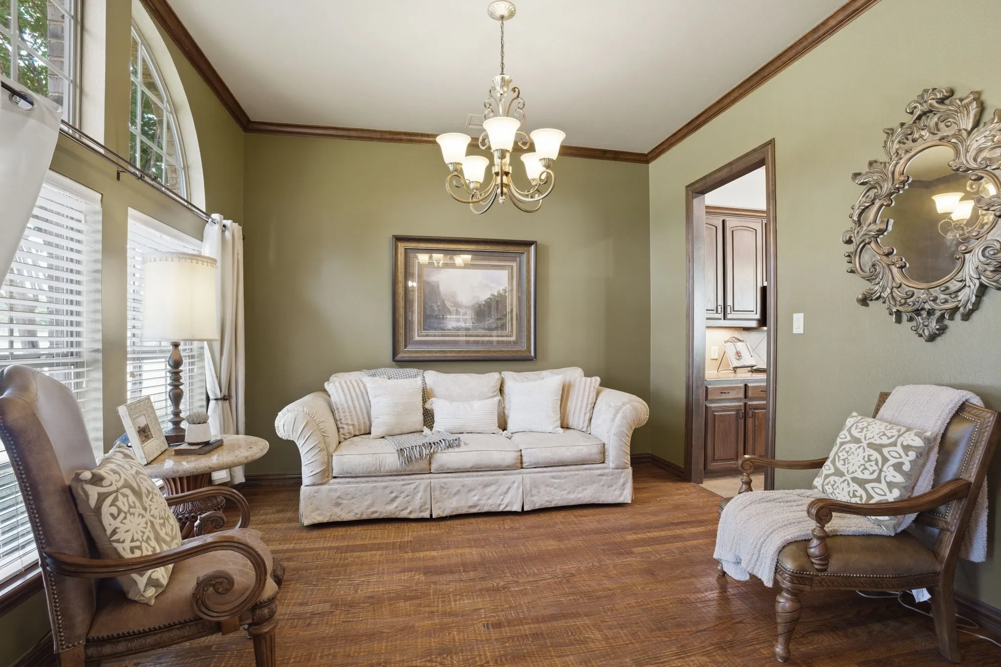The formal dining room features rich wood floors, a large arched window with front yard views, and a centrally positioned chandelier that anchors the space. Versatile in design, it can also serve as a formal living area or a music/piano room.