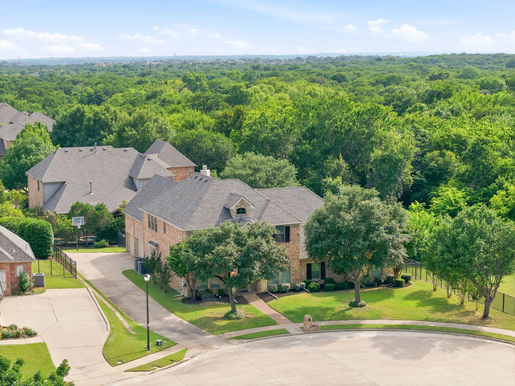 The home showcases a beautifully landscaped front yard framed by mature trees, while the exterior features classic brick accented with window shutters and a striking stone archway flanked by lantern lights on each side, gracefully welcoming you to the front porch.