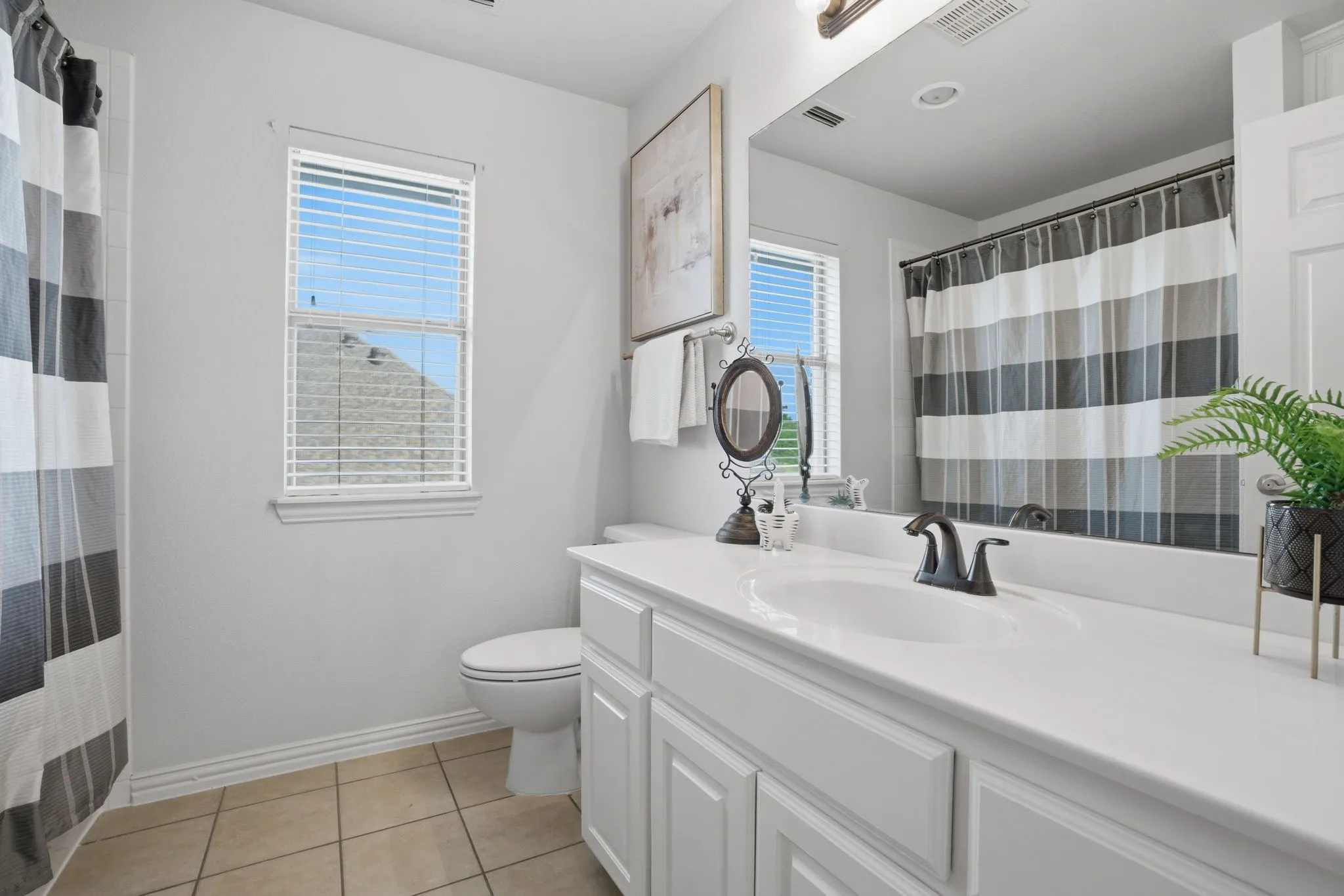 Bathroom 4 is a full bath featuring tile flooring and a built-in white vanity accented with brushed bronze fixtures. A window brings in natural light, enhancing the bright and airy feel. The tub/shower combination is finished with a white tile surround and a Pfister shower system, while custom floor-to-ceiling linen cabinetry provides exceptional storage.
