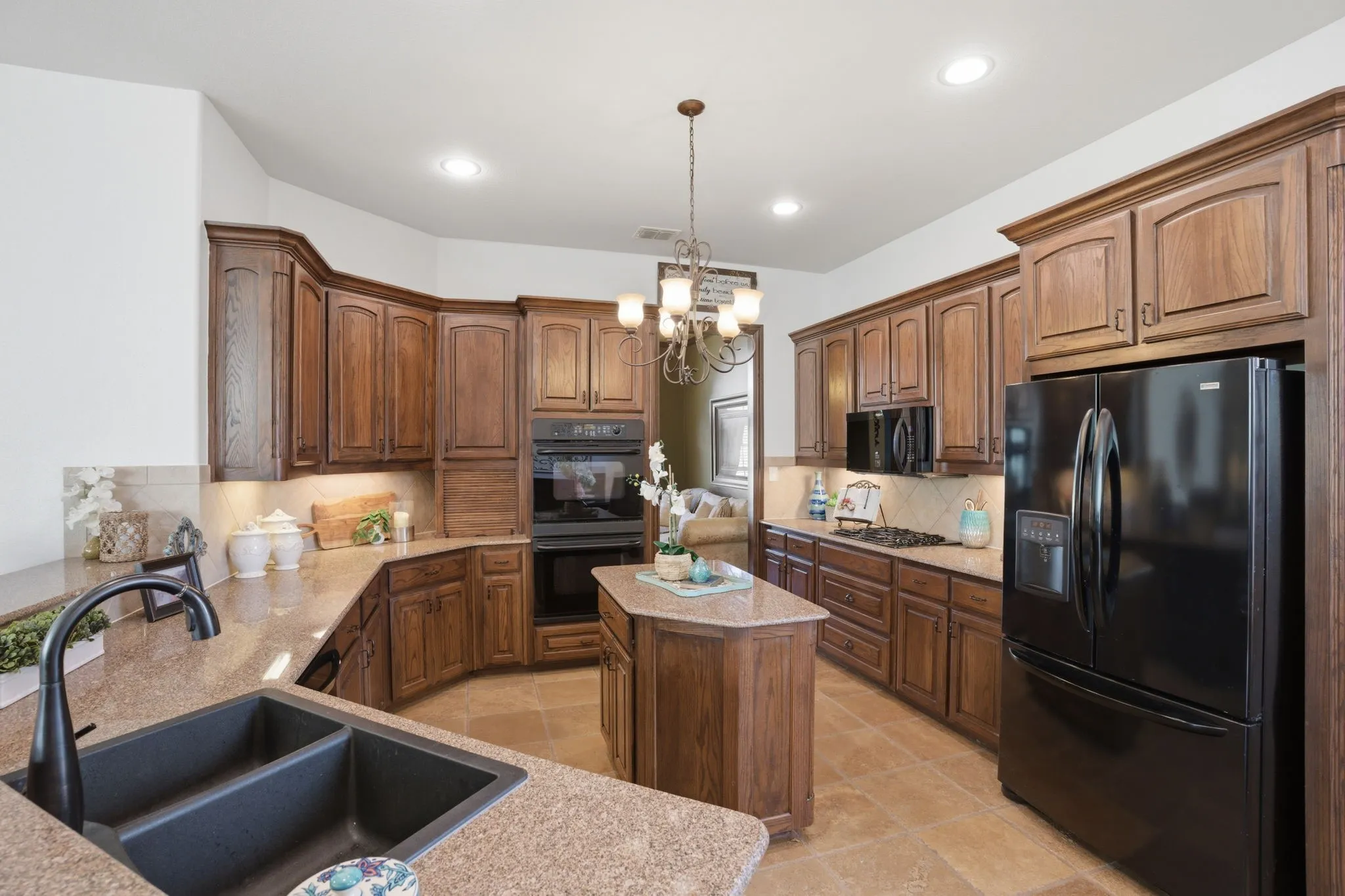 The eat-in kitchen is both stylish and functional, featuring a spacious breakfast bar with ample space for barstool seating, freshly sealed travertine flooring, and warm wood cabinetry paired with granite countertops and a tile backsplash.