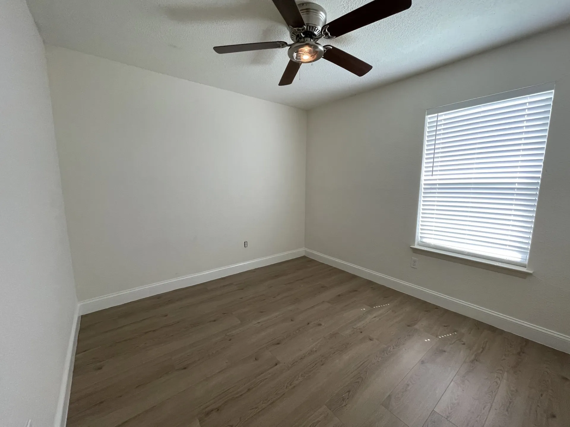 Room featuring wood-finish flooring, white baseboards, and a window with blinds