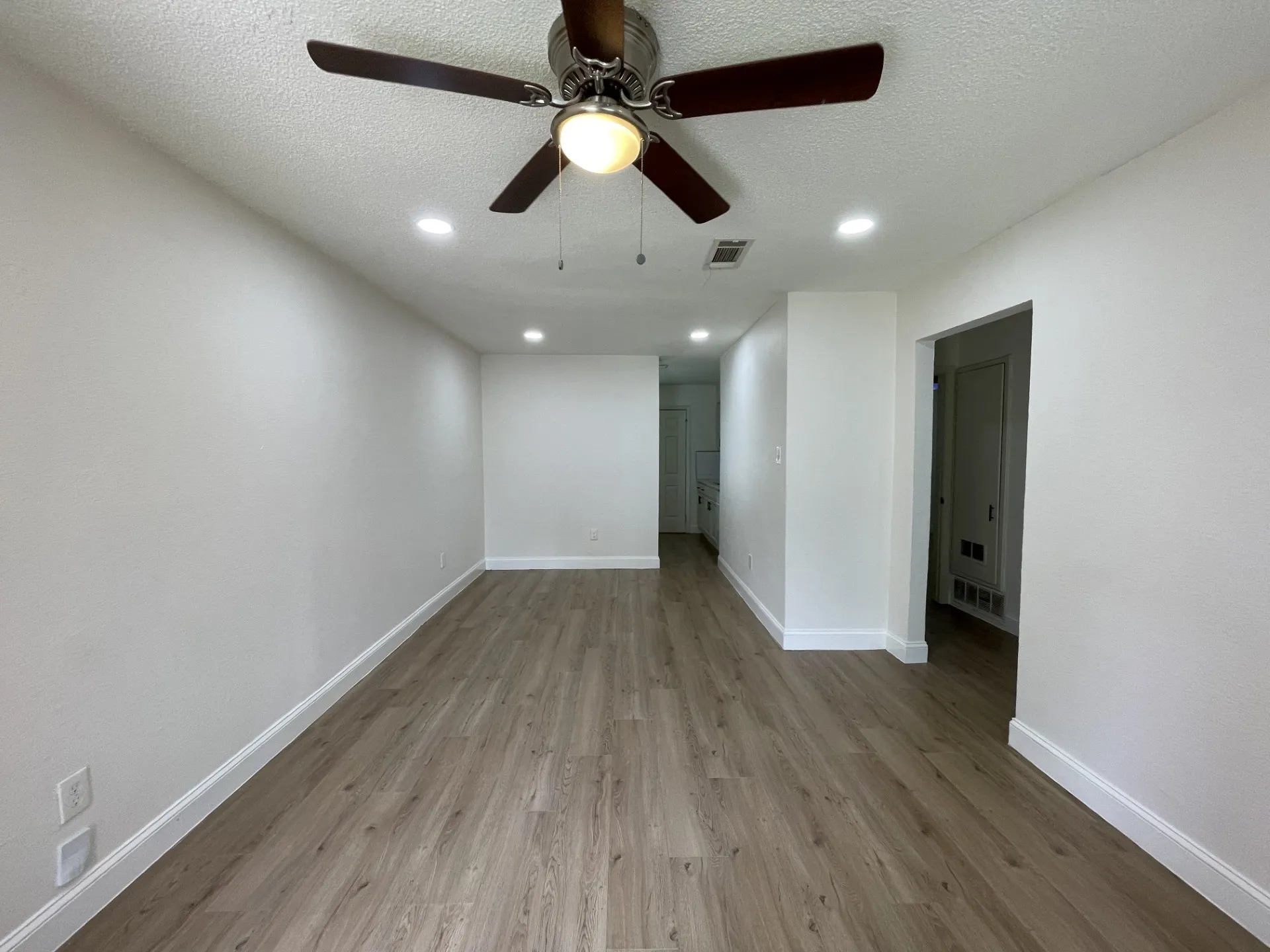 Spacious room featuring wood-finish flooring, white baseboards, recessed lighting, and a ceiling fan with integrated light