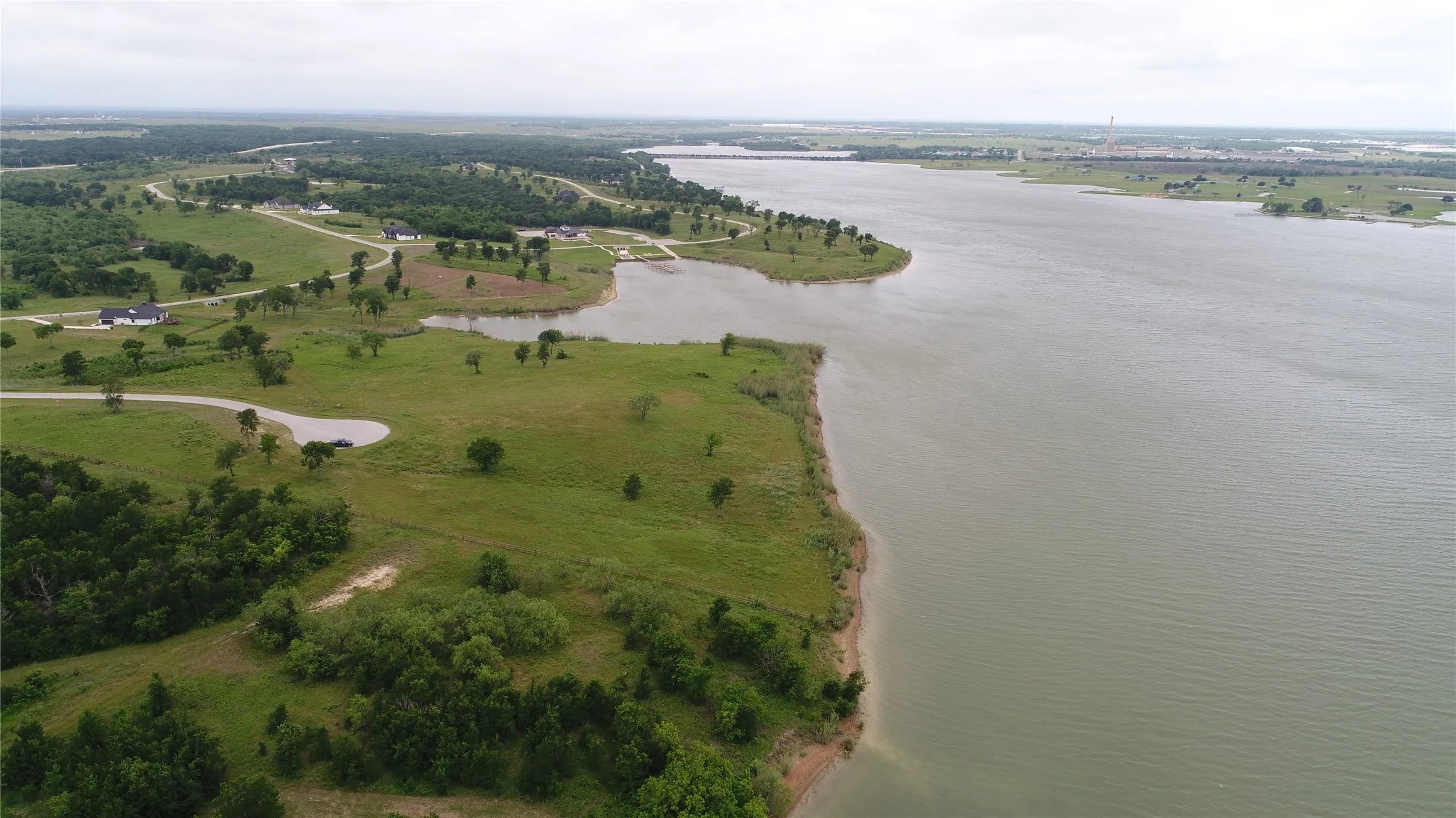 Expansive waterfront property featuring a substantial body of water, green landscape, scattered trees, and visible residential structures