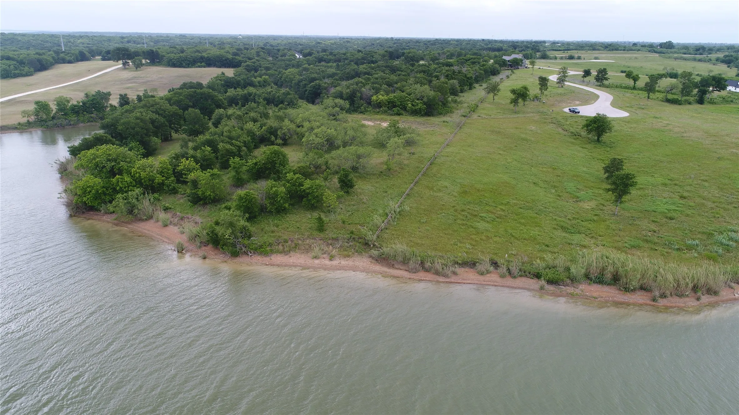Expansive waterfront lot featuring a natural shoreline, mature trees, and a partially paved road