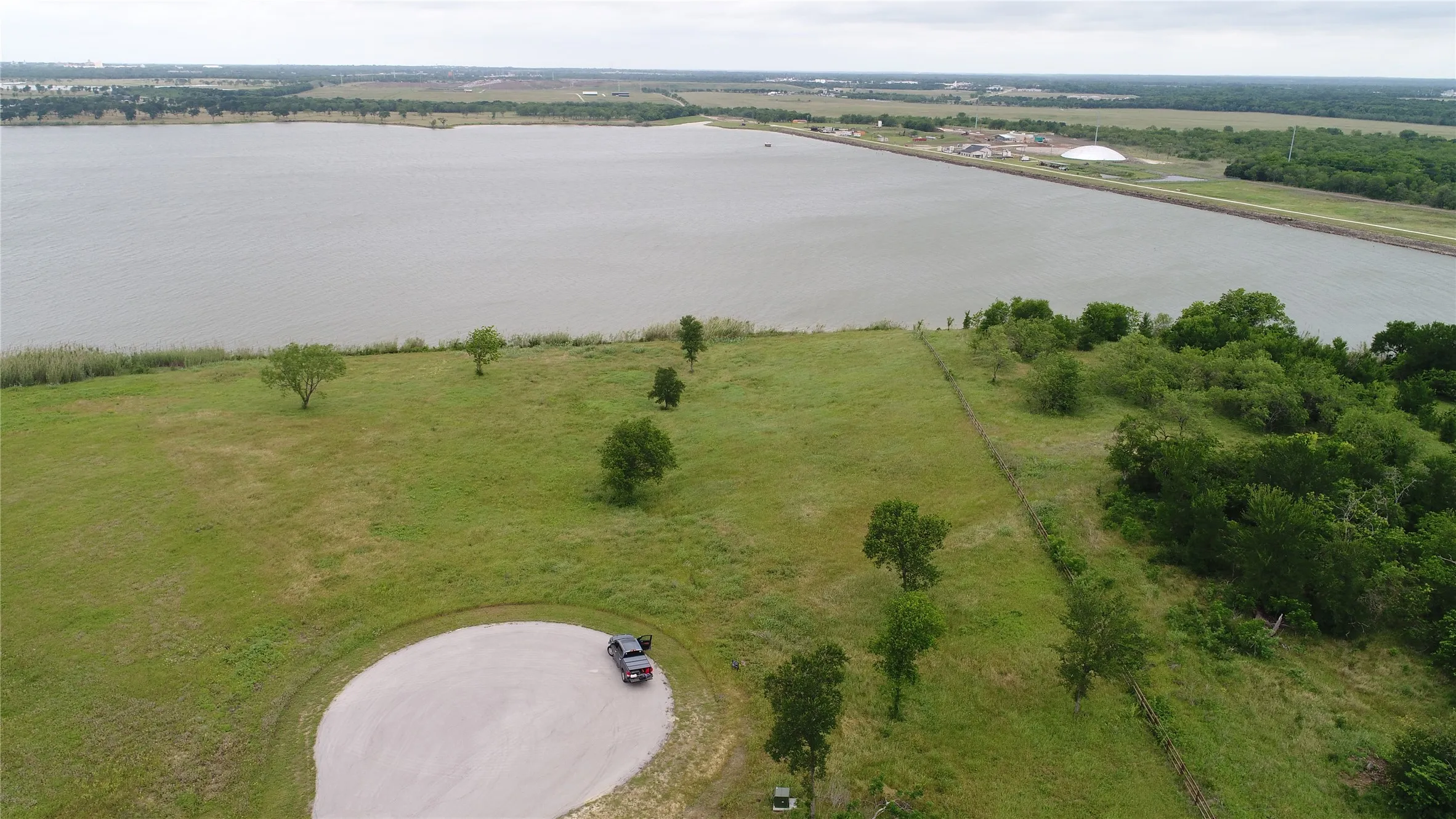 Grassy terrain featuring scattered trees and a water body in the background