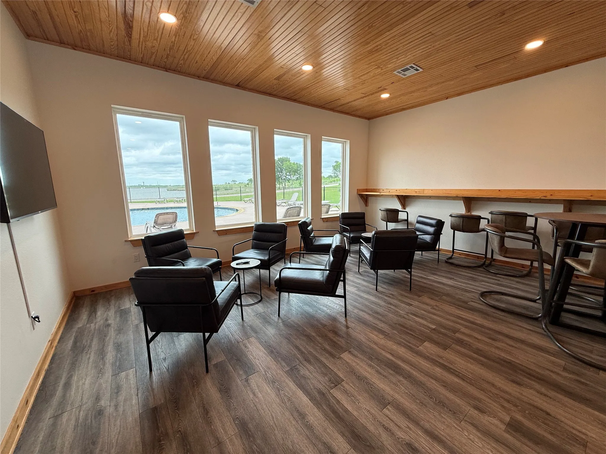 Clubhouse with spacious meeting or party room featuring a wood-panel ceiling with recessed lighting, multiple windows, wood-finish flooring, and a built-in wall shelf.