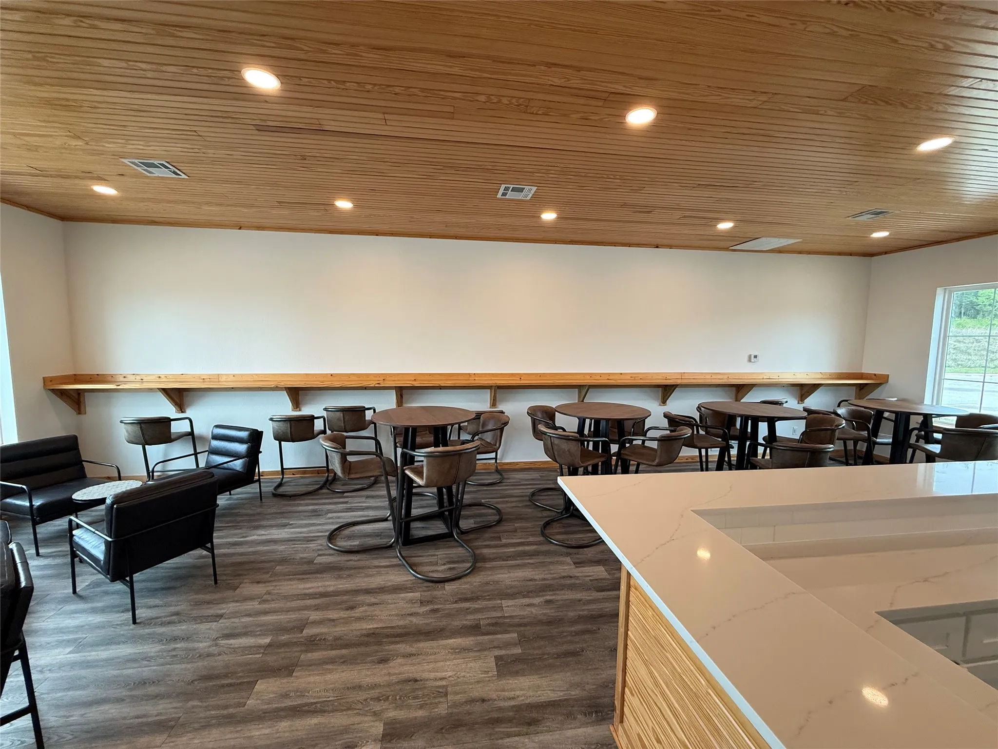 Open clubhouse with spacious interior featuring wood-finish ceiling, recessed lighting, a long built-in wood shelf, wood-finish flooring, and a large window overlooking the pool.