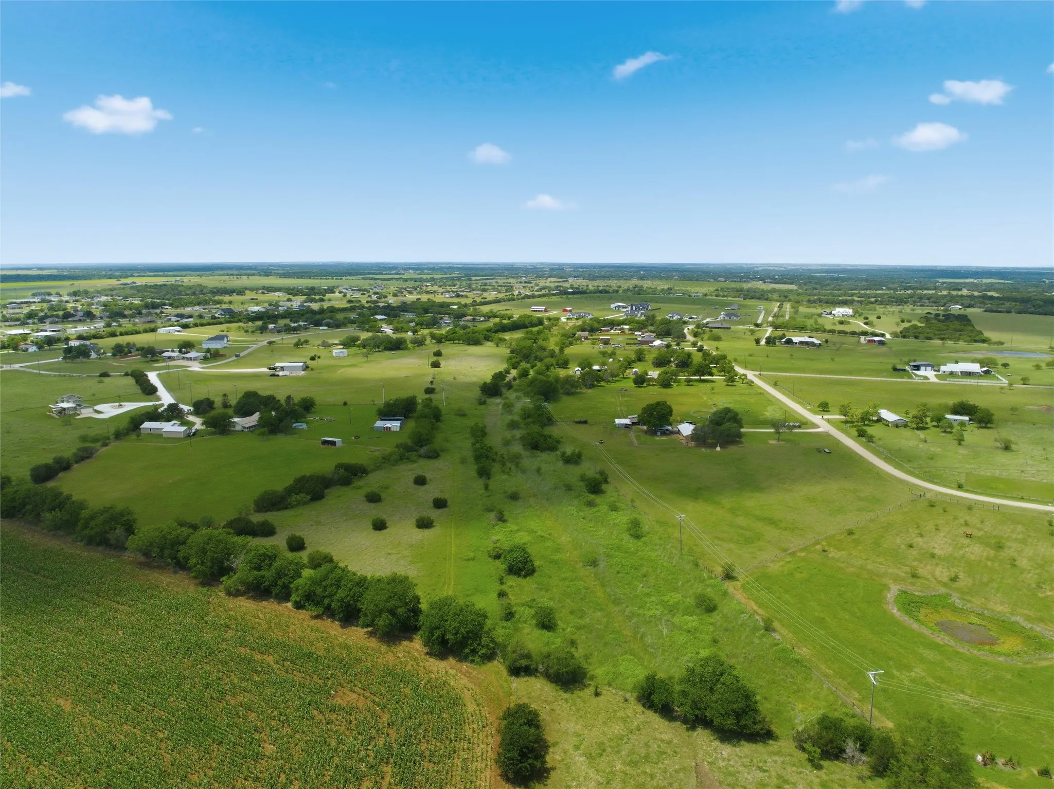 Expansive green acreage featuring scattered homes, established trees, and a distant body of water