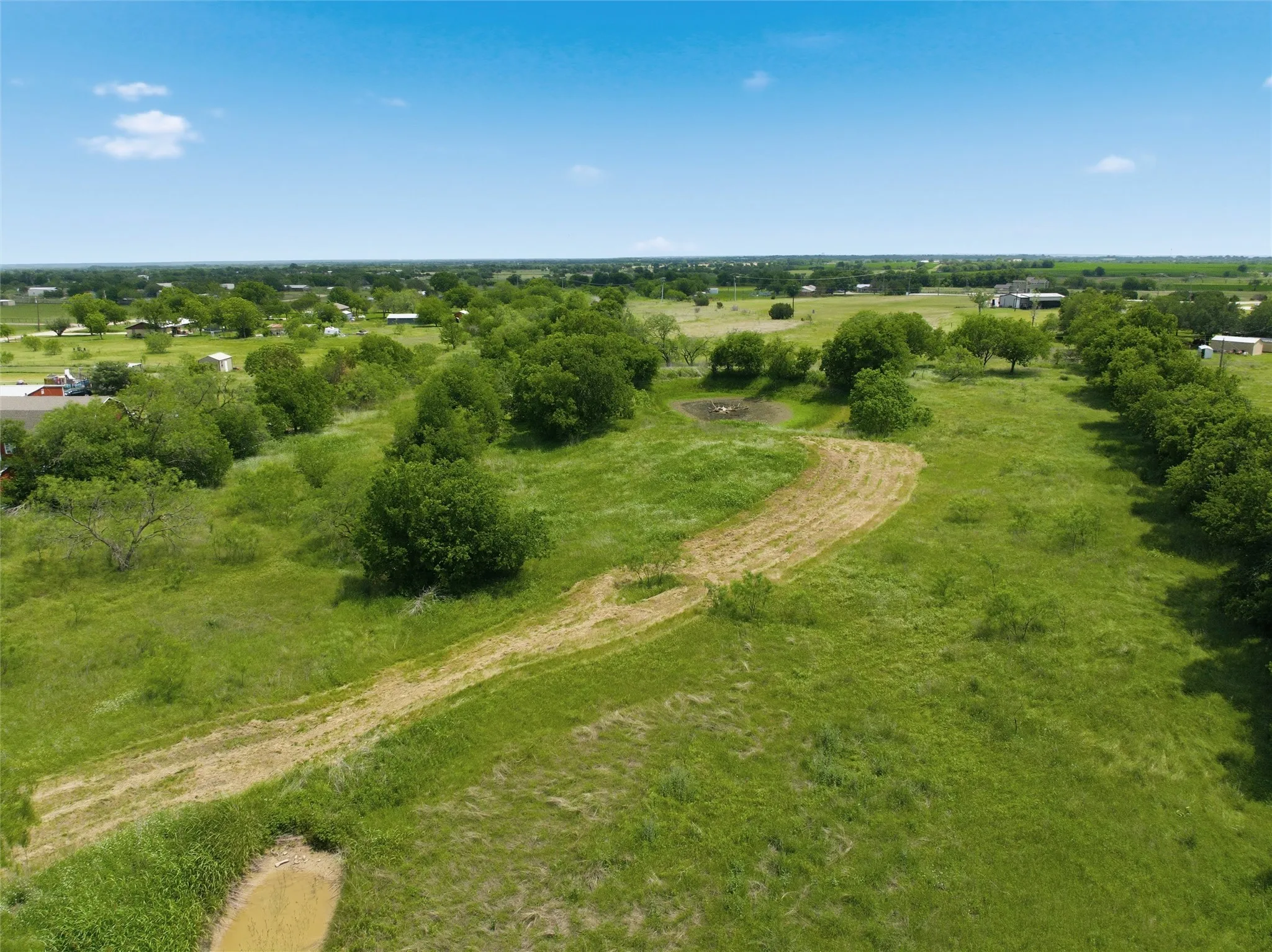 Expansive green landscape featuring mature trees, a cleared path, and a small pond