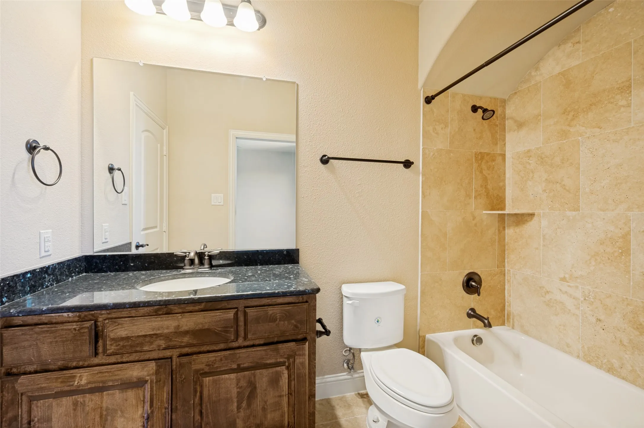 Private ensuite bathroom featuring a granite-topped vanity with rich wood cabinetry, elegant tile flooring, and a tiled tub/shower combination. Designed with comfort and convenience in mind, this well-appointed bath provides the perfect private space for family members or overnight guests.