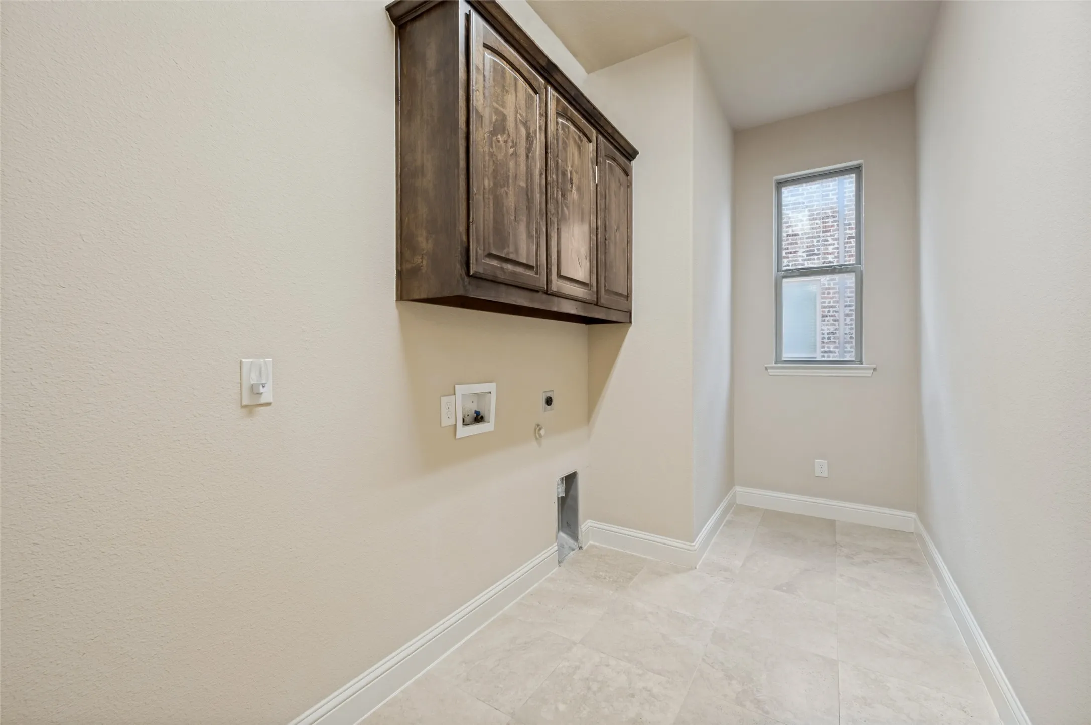 Functional laundry room featuring upper cabinetry for convenient storage, durable tile flooring, and space for a full-size washer and dryer. A large window brings in natural light, making everyday chores more enjoyable while keeping the space bright and inviting.