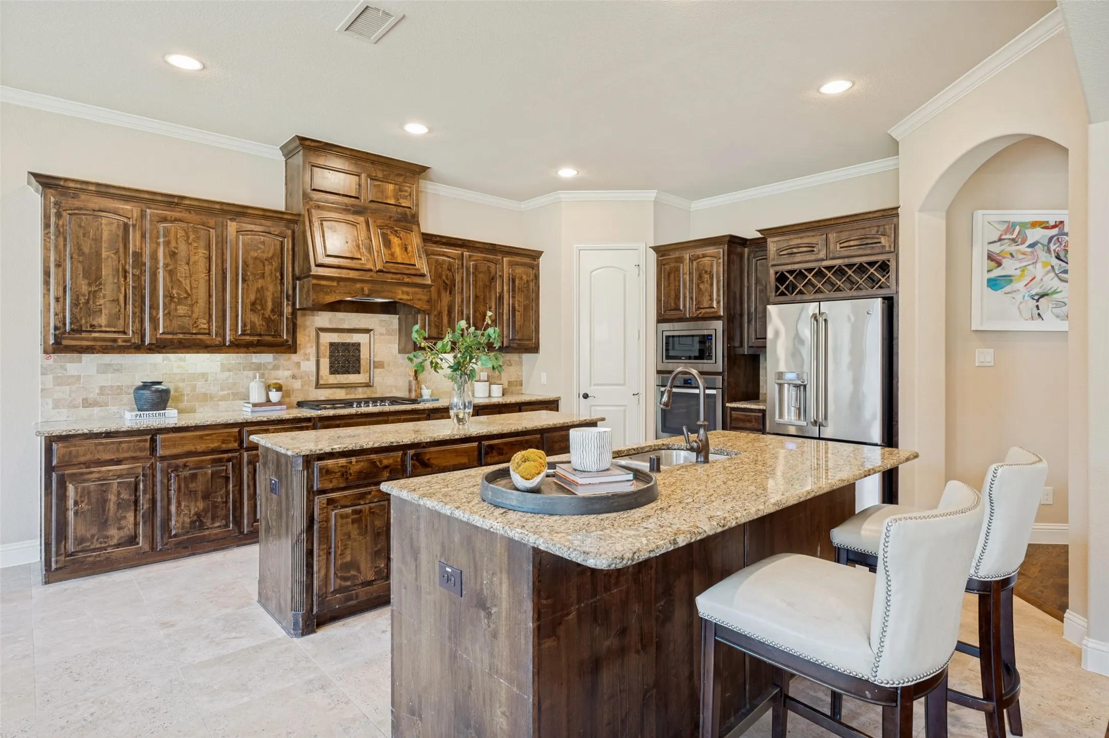 A chef's dream, this gourmet kitchen showcases rich custom wood cabinetry, granite countertops, dual oversized islands, stainless steel appliances, double ovens, a gas cooktop with a custom vent hood, and a built-in wine rack. Designed for both everyday living and effortless entertaining, the open layout offers abundant prep space, generous storage, and seamless flow into the spacious family room.