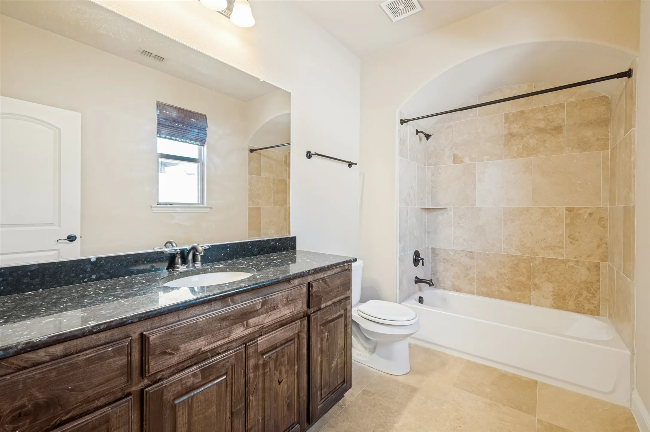 Private ensuite bathroom featuring a granite-topped vanity with rich wood cabinetry, elegant tile flooring, and a tiled tub/shower combination. Designed with comfort and convenience in mind, this well-appointed bath provides the perfect private space for family members or overnight guests.