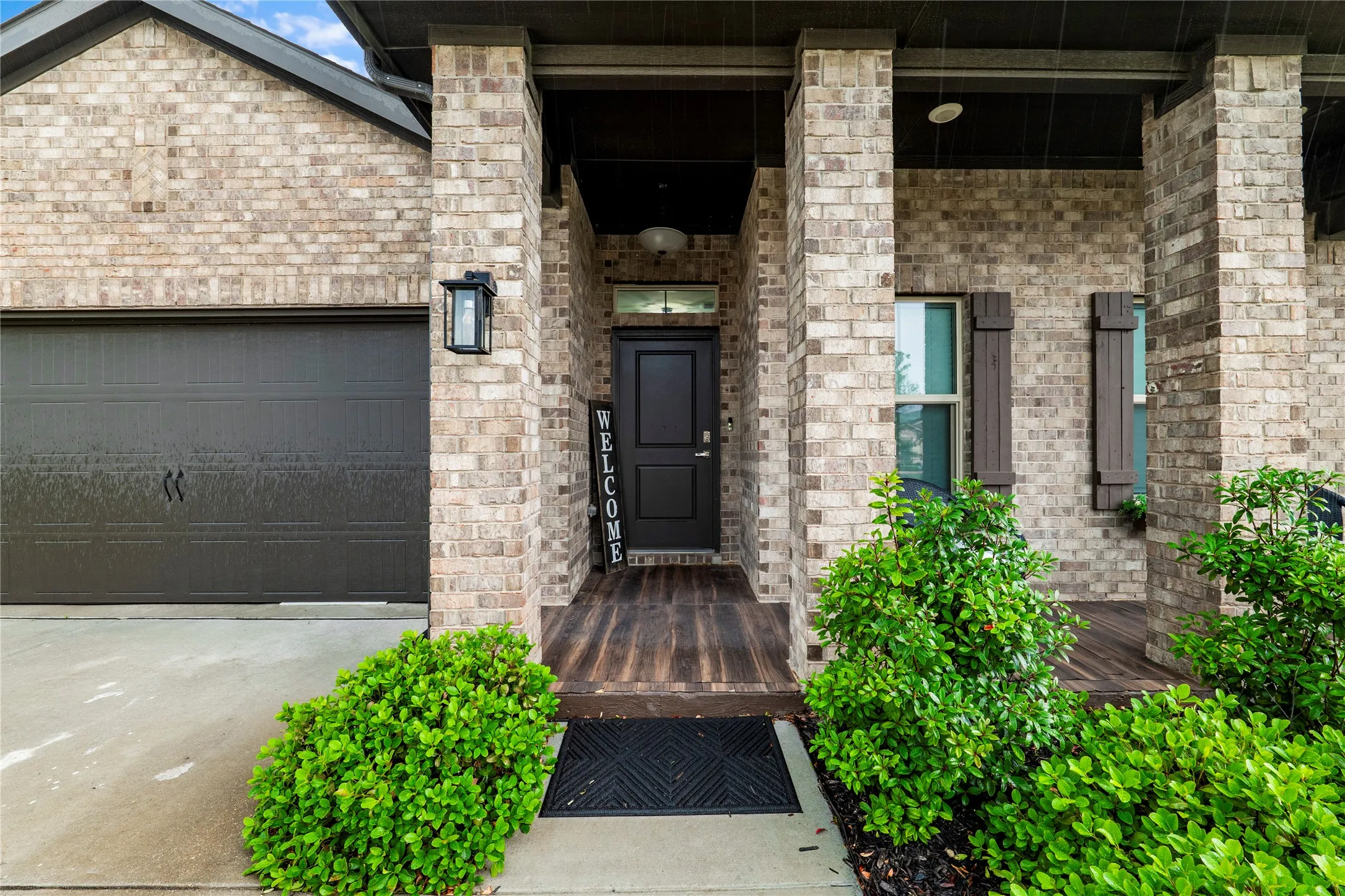 Brick exterior featuring a covered porch, dark entry door, and matching garage door