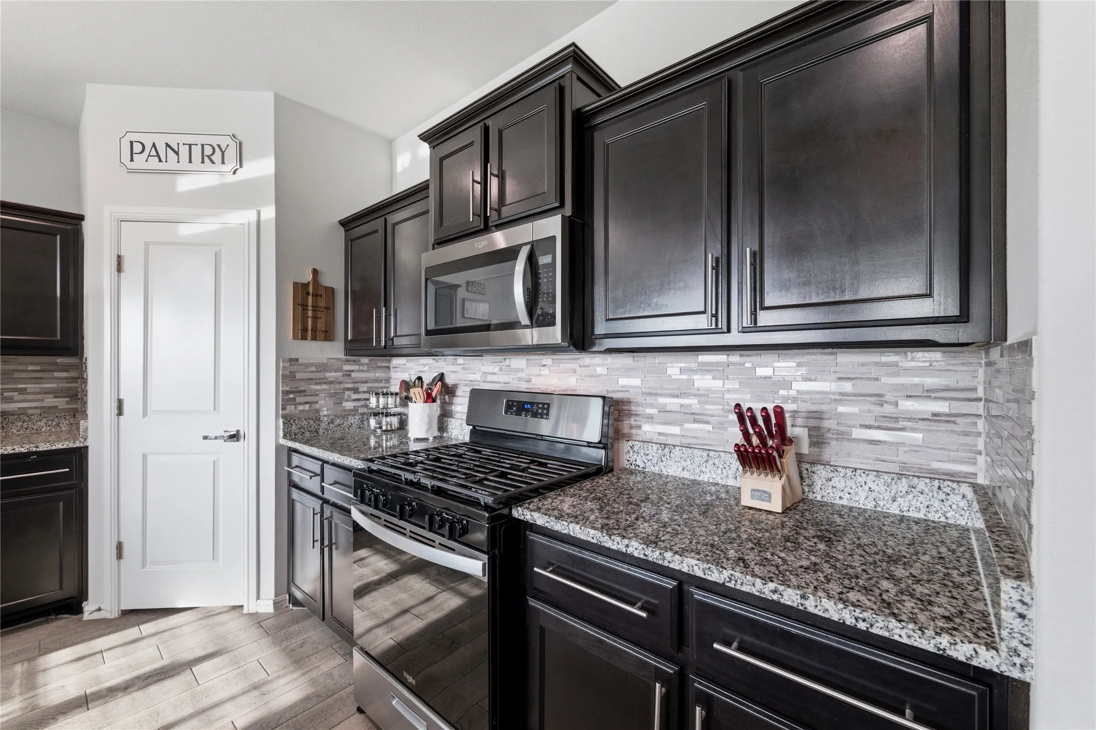 Modern kitchen featuring dark wood-finish cabinetry with silver-tone hardware, granite countertops, and a full-height mosaic tile backsplash