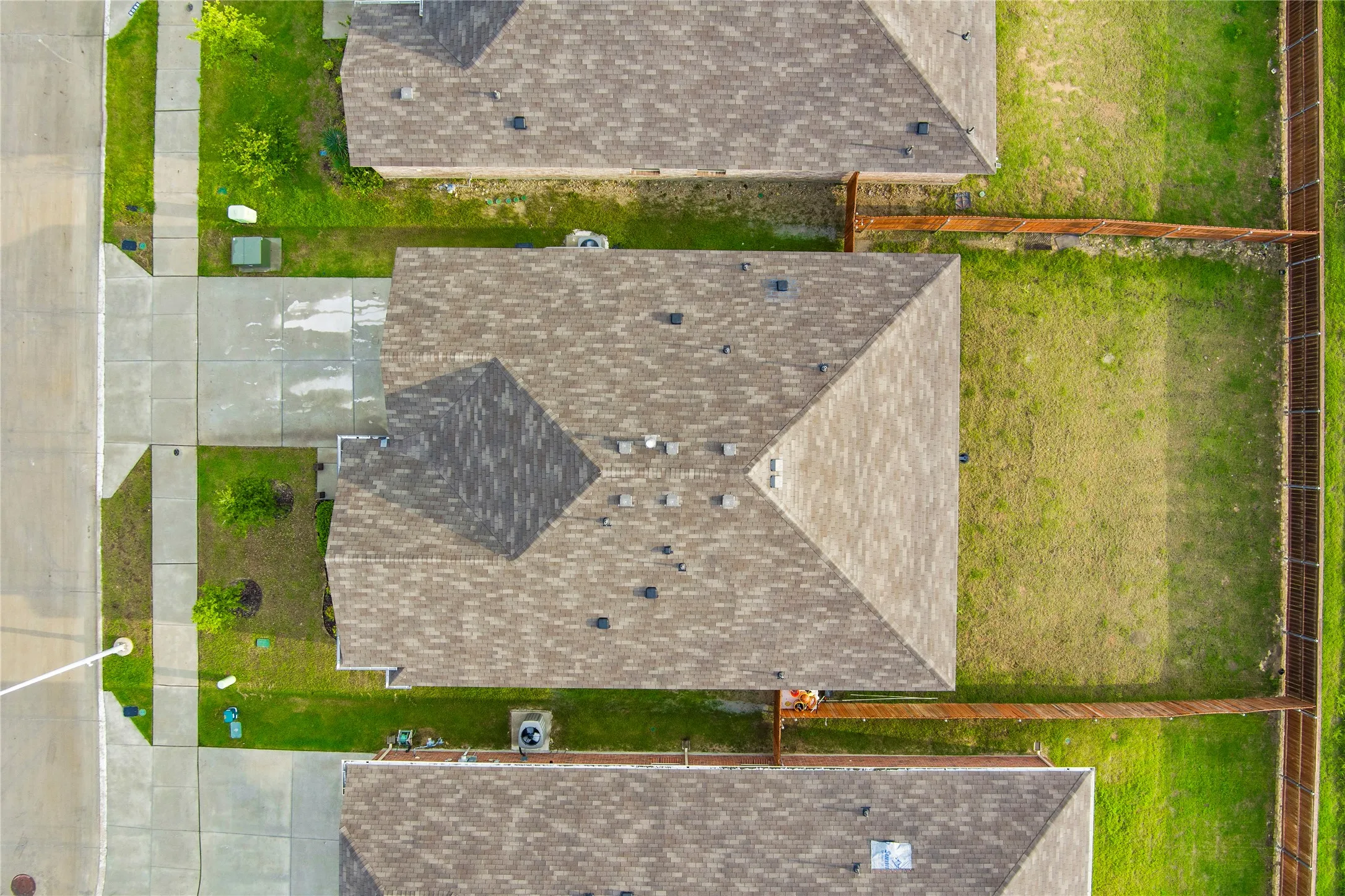 Aerial perspective showcasing a residential property with a shingled roof, concrete driveway, and a fenced backyard