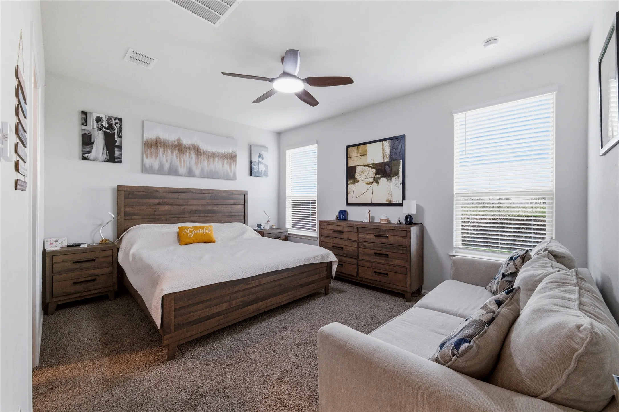 Spacious bedroom featuring neutral wall tones, two windows with blinds, and recessed lighting