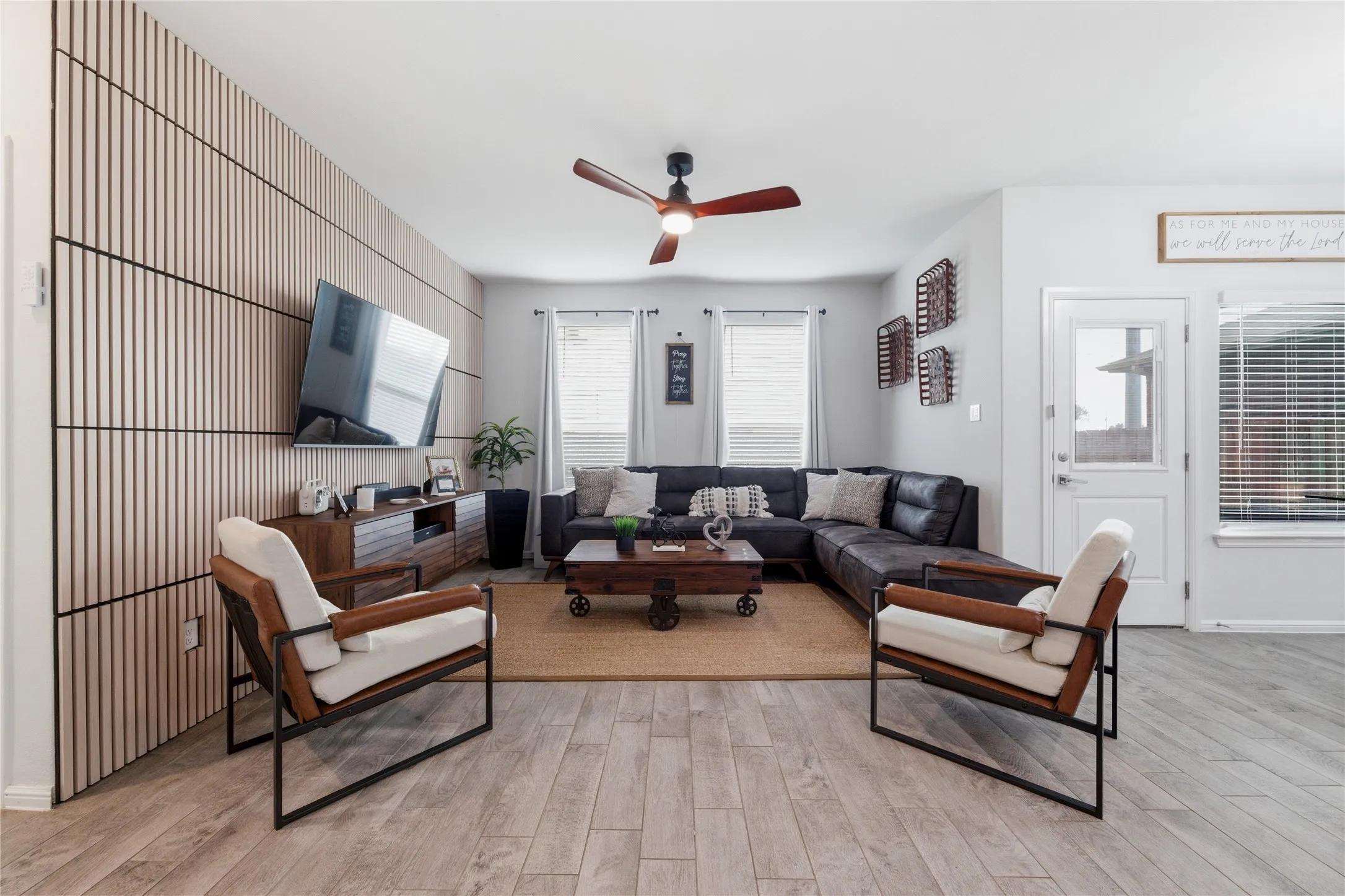 Living area featuring a slatted accent wall, wood-finish flooring, ceiling fan, and window blinds