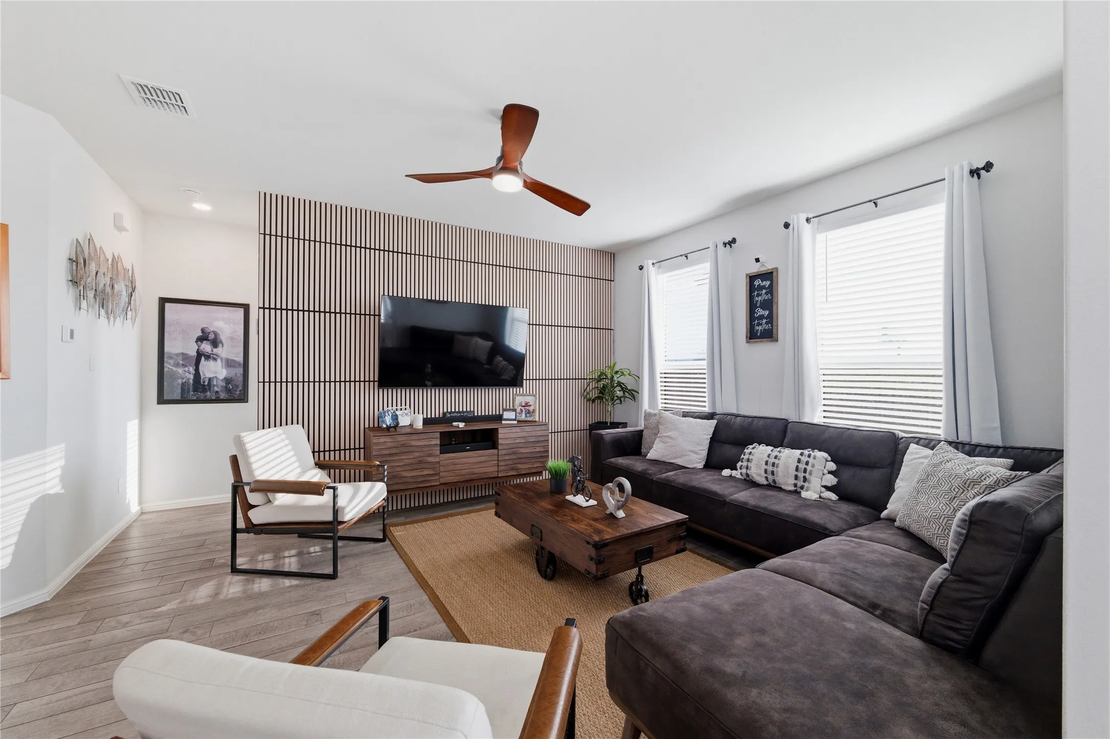 Spacious open-concept living area featuring a decorative slat wall, wood-finish flooring, and a ceiling fan with integrated lighting