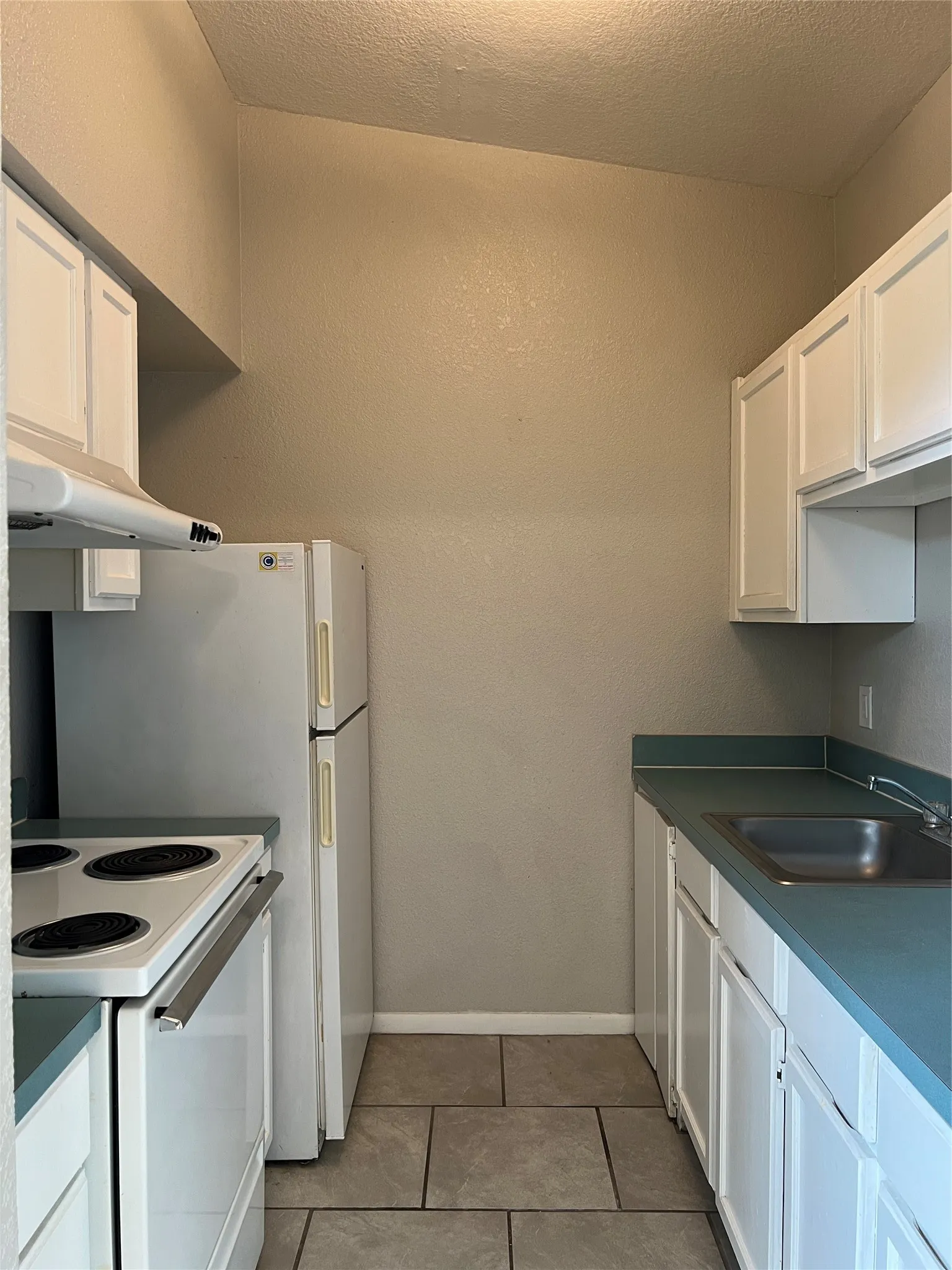 This view of the kitchen shows the stainless steel sink and white appliances. Notice all of the cabinet space.