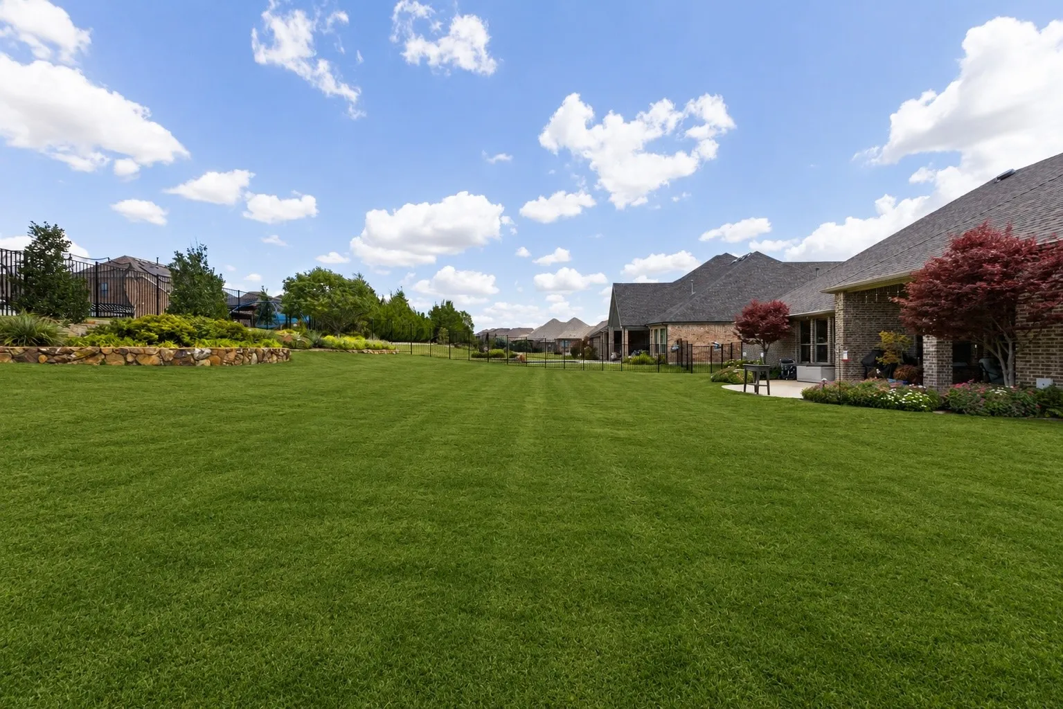 Expansive lawn with mature landscaping, a stone retaining wall, and a covered patio area. Plenty of room for a large pool!