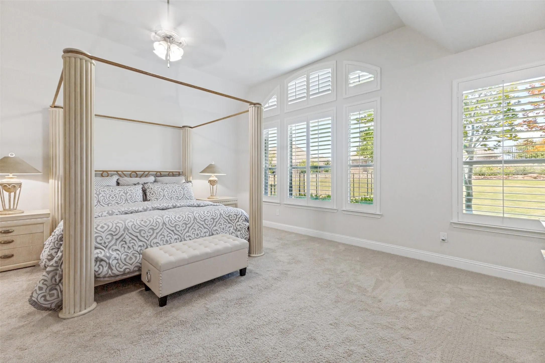 Find vaulted ceilings, multiple windows with plantation shutters, and a ceiling fan in the large Primary Suite, located at the back of the home.