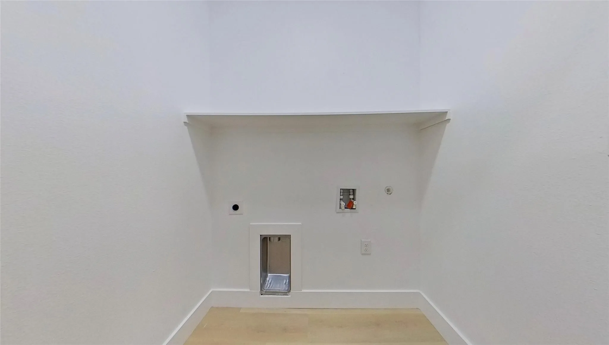 Dedicated laundry alcove featuring light wood-finish flooring, white baseboards, and a built-in shelf