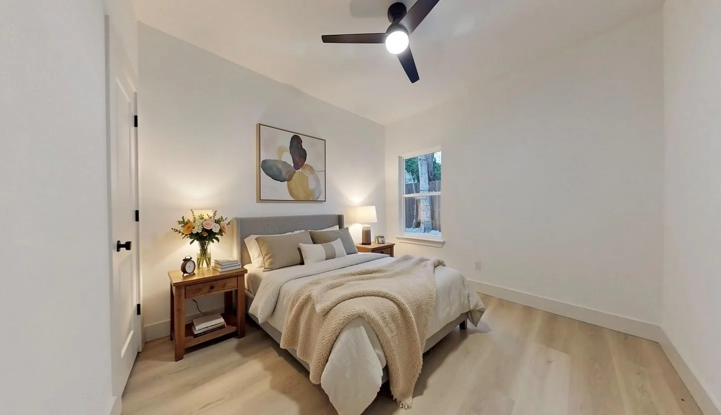 Bedroom featuring light wood-finish flooring, a contemporary ceiling fan with integrated lighting, a window providing natural light, and a white paneled door
