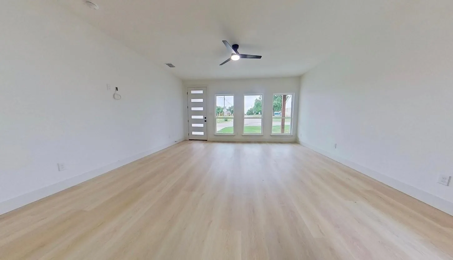 Spacious room featuring light wood-finish flooring, white walls, and a modern ceiling fan