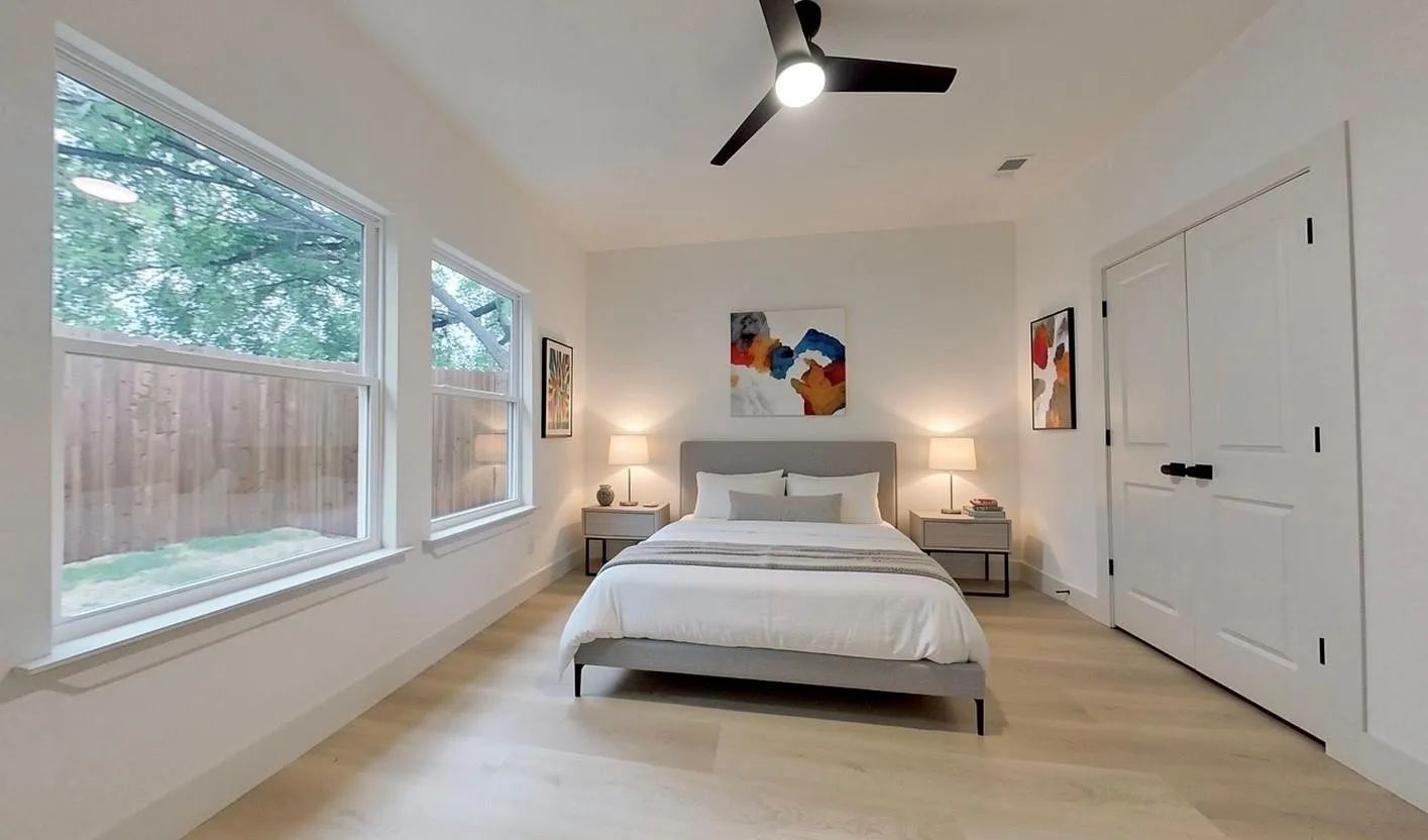 Naturally illuminated room featuring two large windows, wood-finish flooring, a ceiling fan with integrated lighting, and white double-panel doors