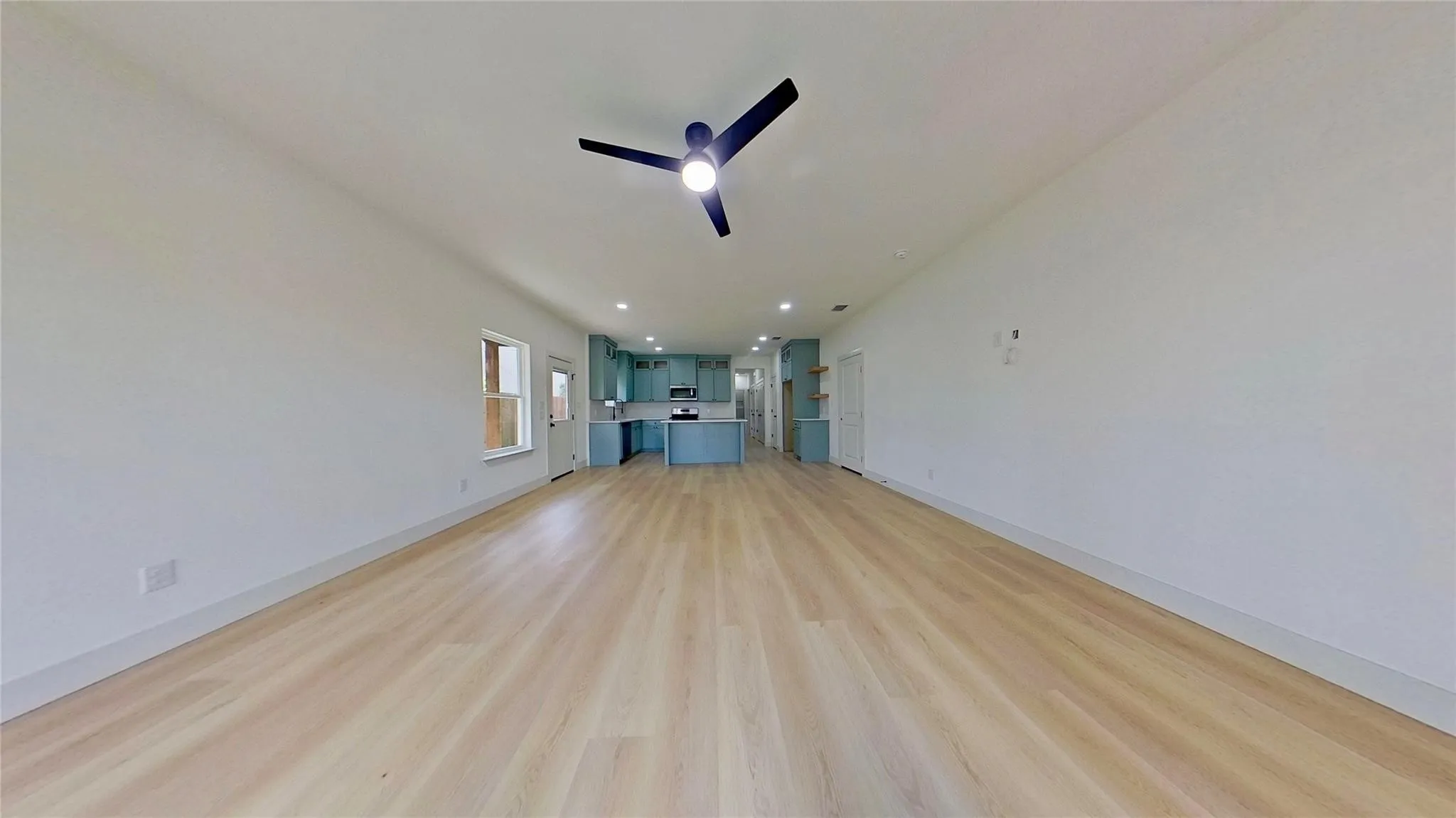 Expansive room featuring wood-finish flooring, light-toned walls, and a contemporary ceiling fan