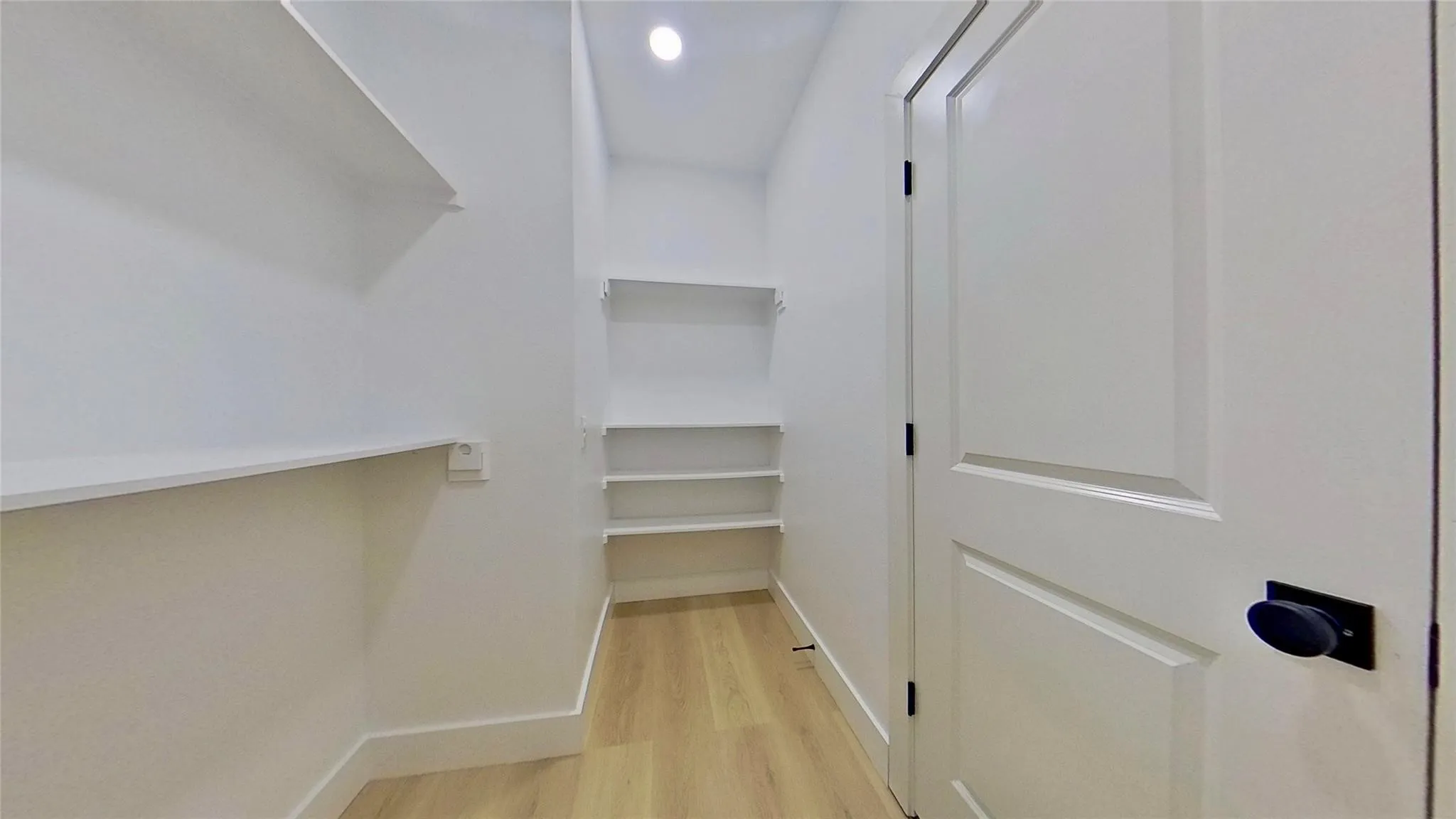 Dedicated pantry featuring extensive built-in shelving, wood-finish flooring, recessed lighting, white trim, and a white paneled door with matte black hardware