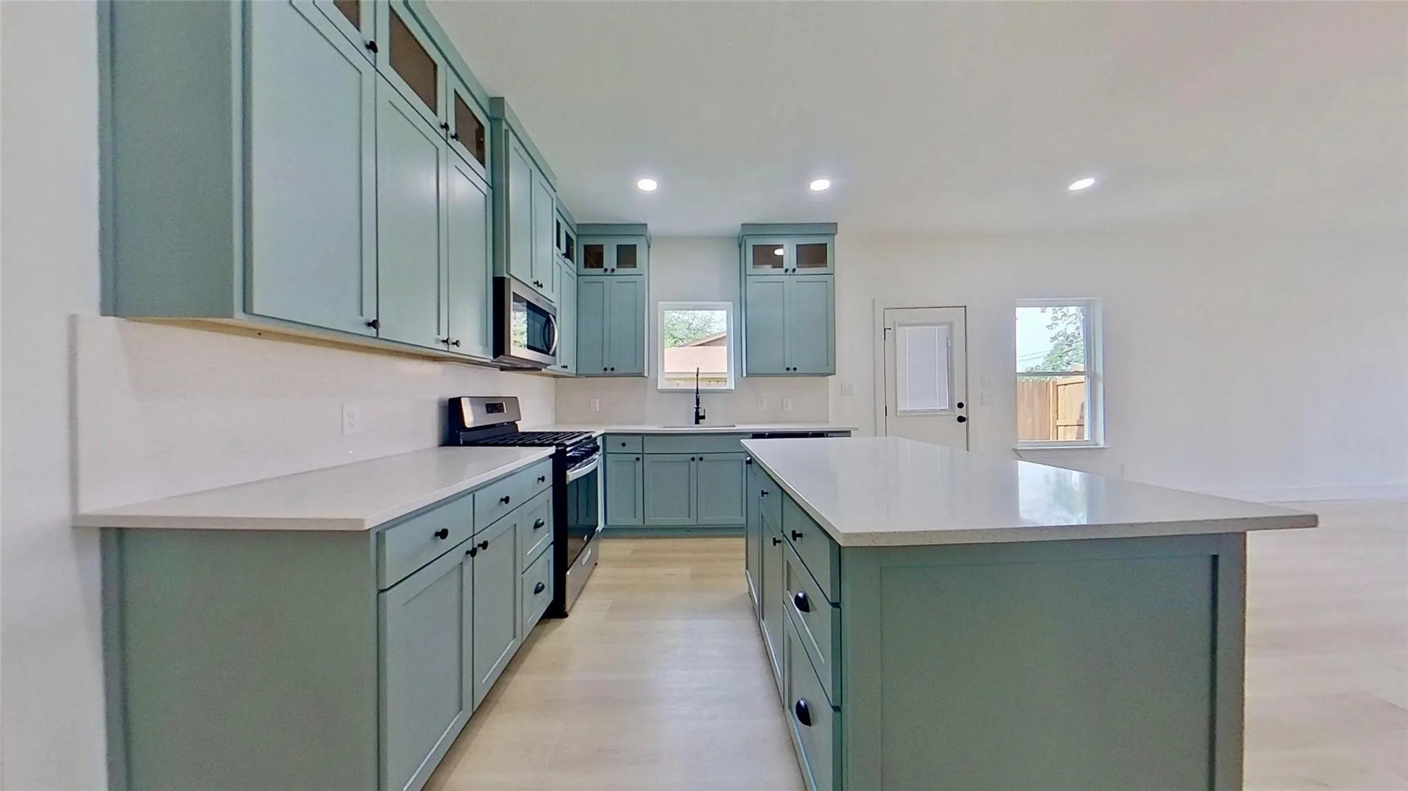 Contemporary kitchen featuring light blue cabinetry, light-toned countertops, stainless steel appliances, and wood-finish flooring