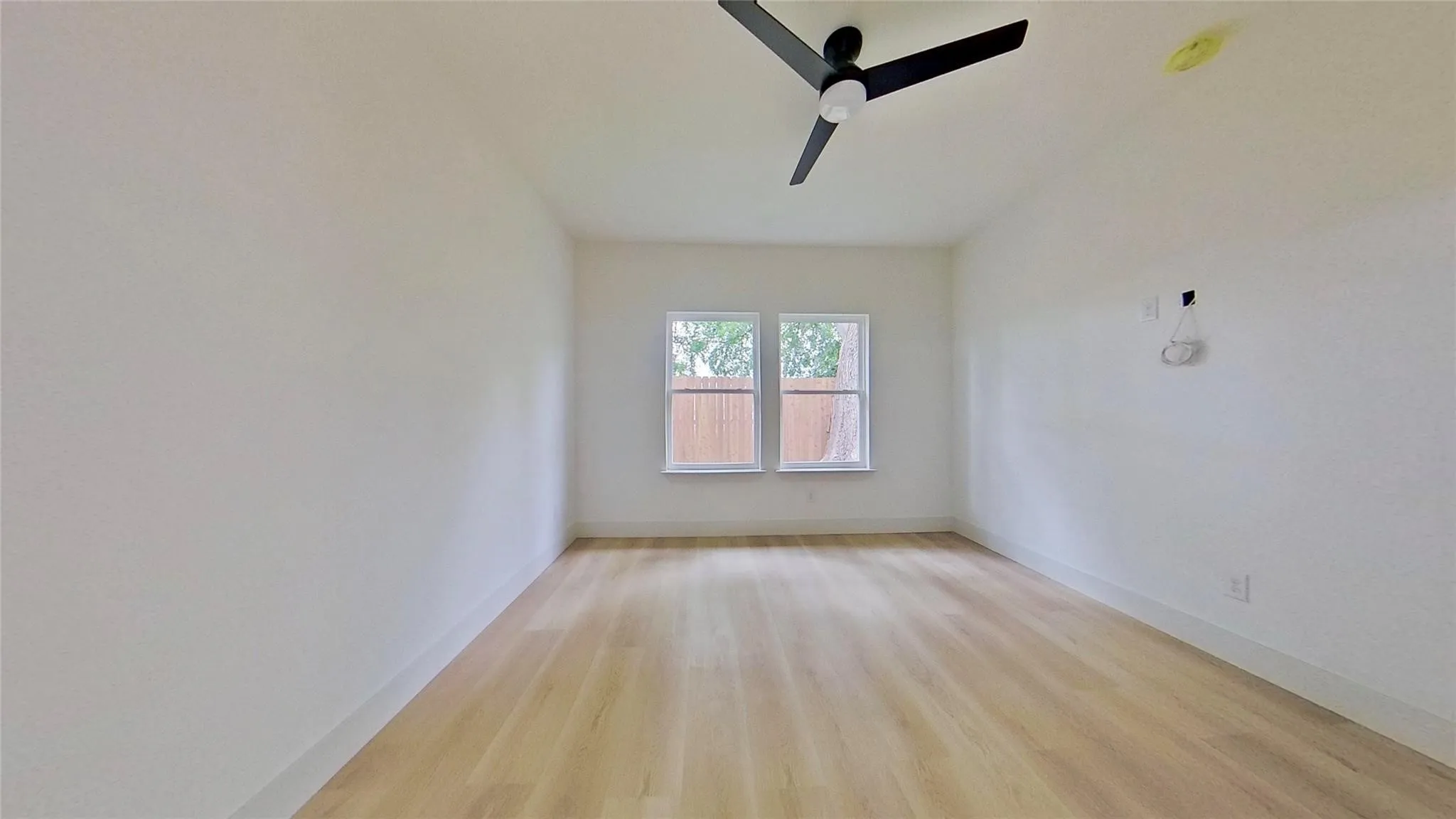 Room featuring light wood-finish flooring, crisp white walls, and a contemporary black ceiling fan