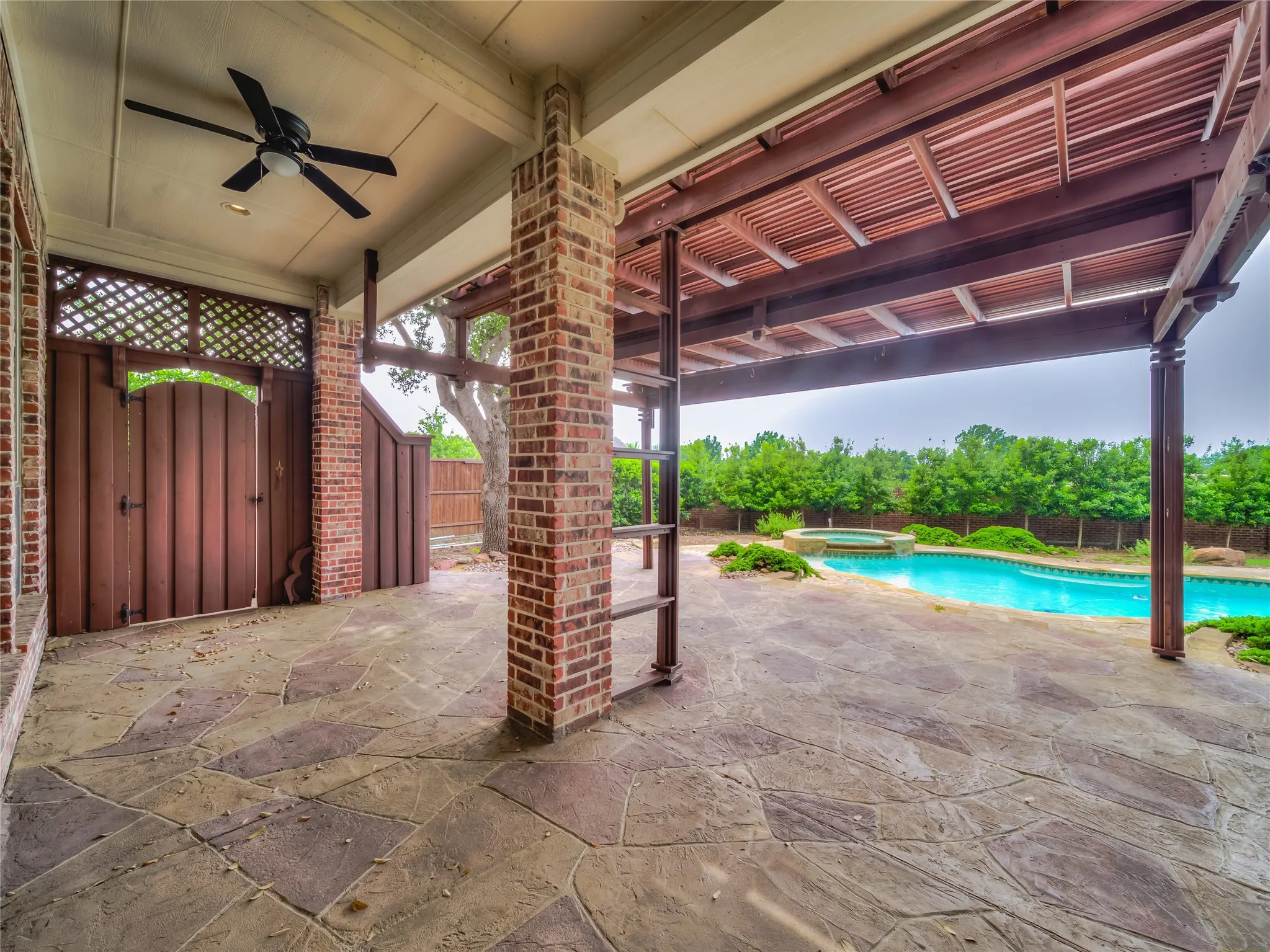 Expansive covered patio featuring a flagstone-style surface, brick columns, a ceiling fan, and a wood lattice privacy screen