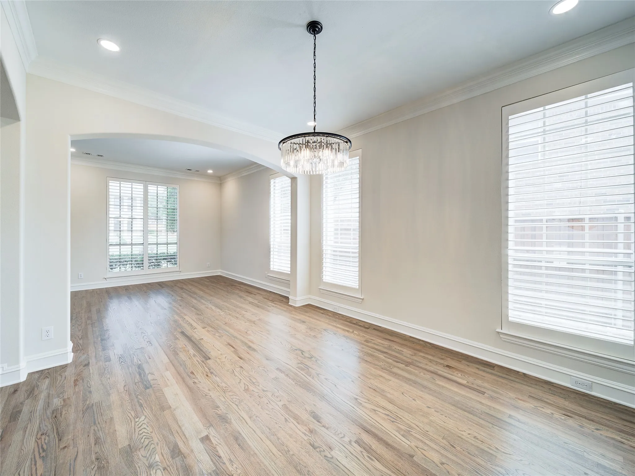Hardwood flooring extends throughout this expansive room, featuring a contemporary chandelier and recessed lighting