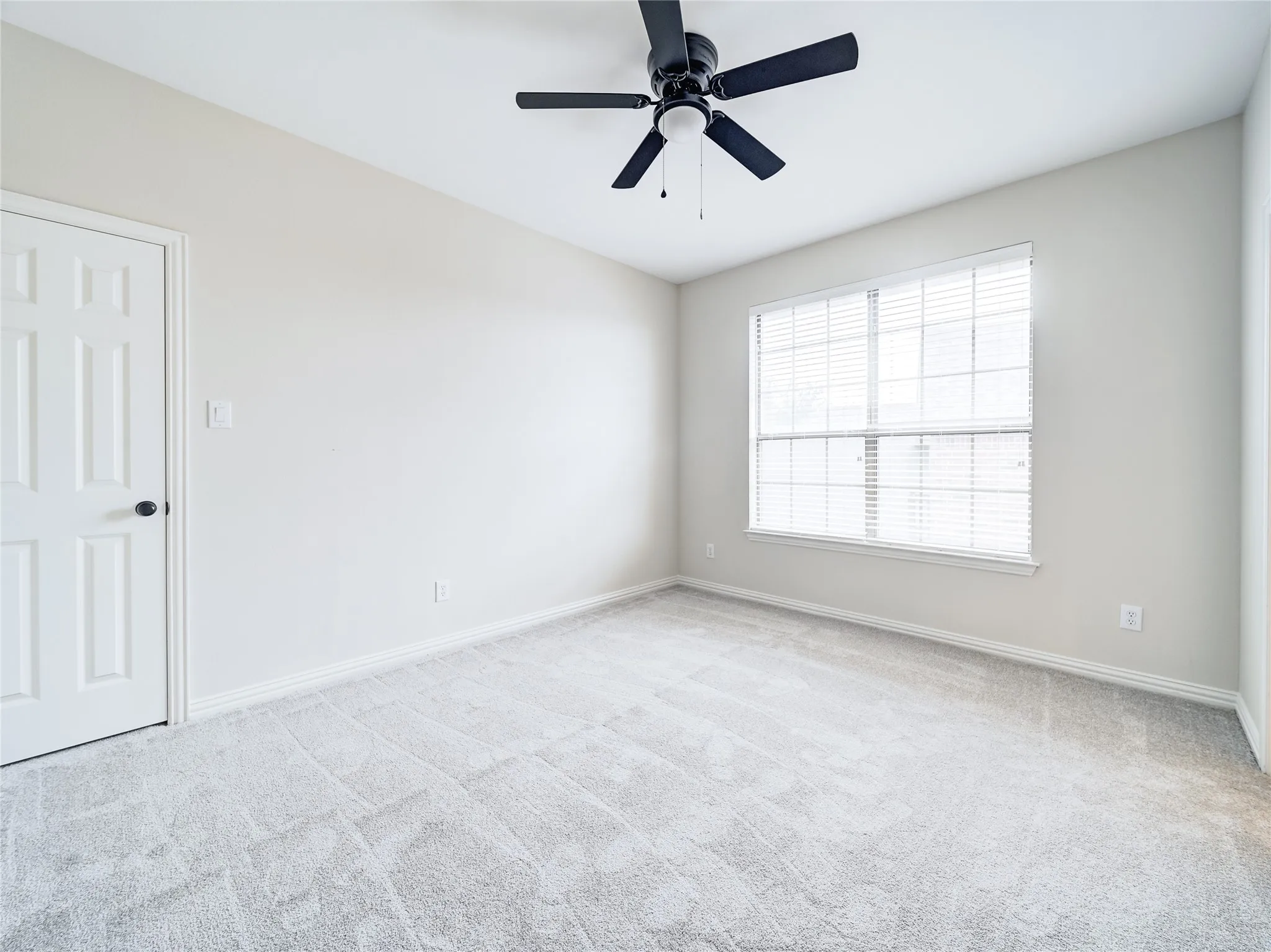 Bright room featuring a large window with horizontal blinds, neutral wall paint, and light-colored carpeting