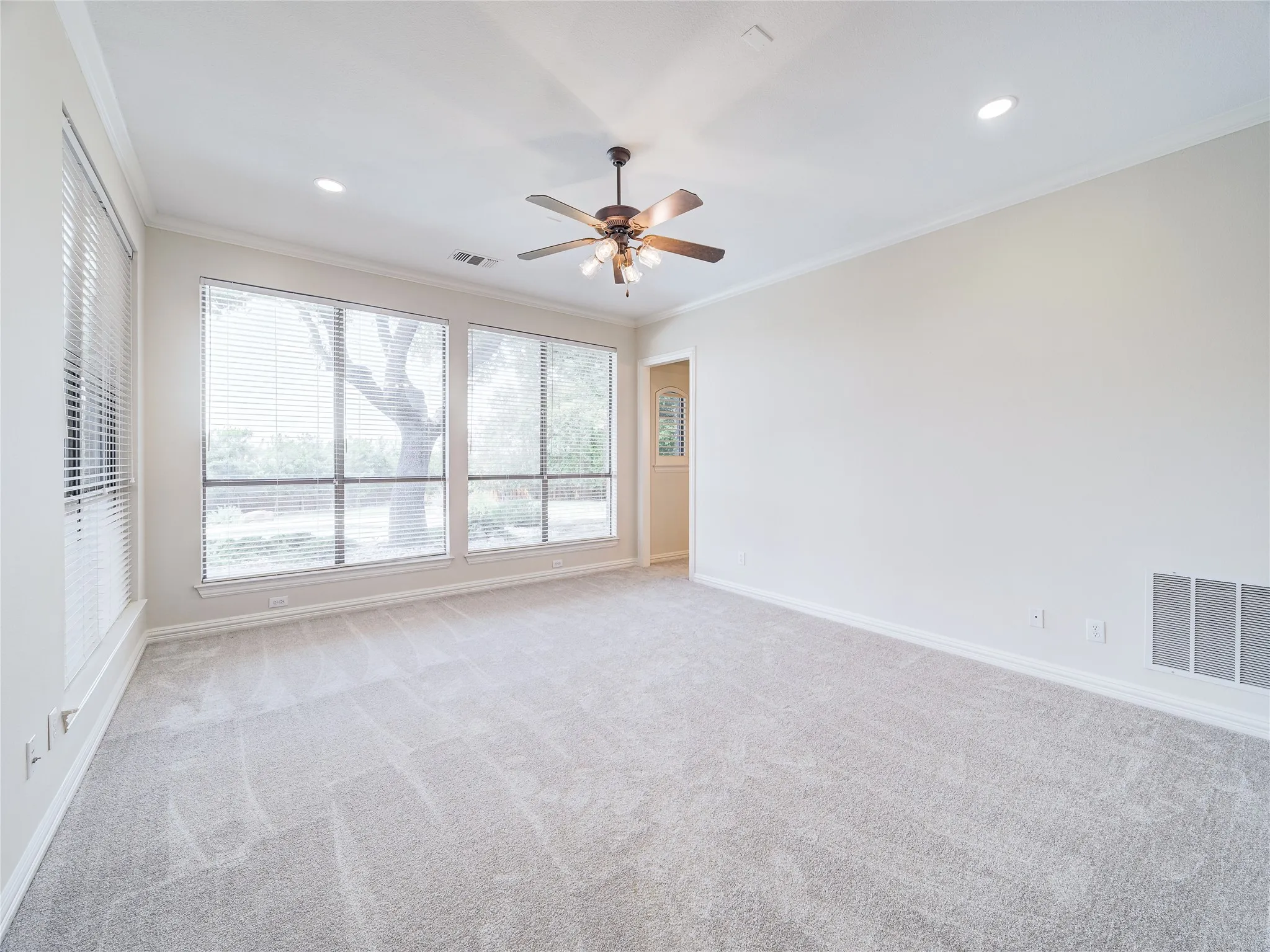 Spacious room featuring multiple large windows with blinds, light gray carpeting, recessed lighting, and a ceiling fan with light fixture