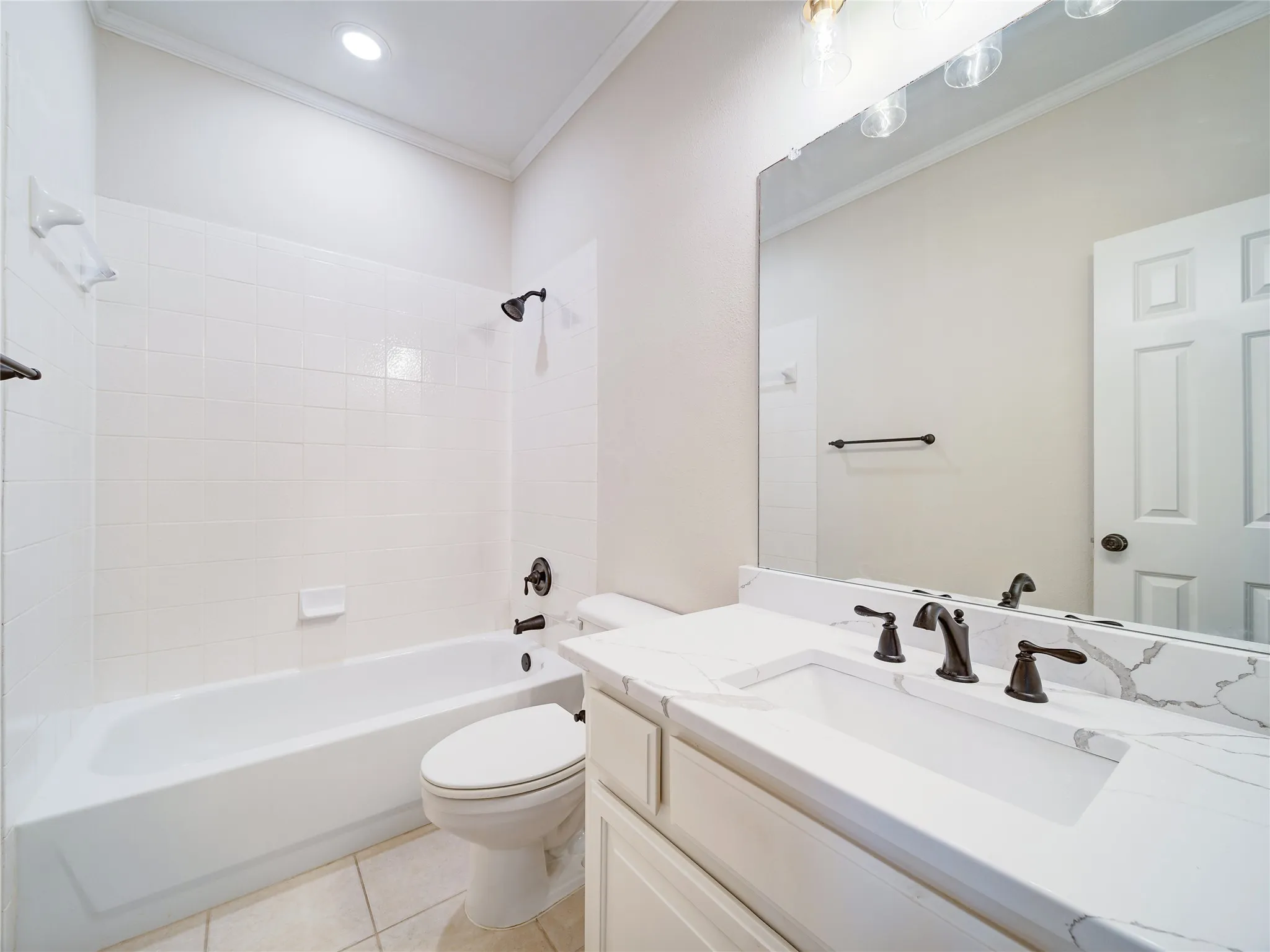 Bathroom featuring a white bathtub with subway tile surround, dark bronze fixtures, a vanity with a white countertop and integrated sink, a large mirror, and recessed lighting