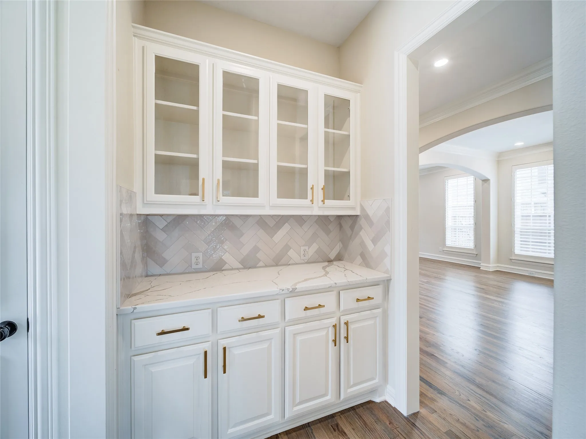 Built-in white cabinetry with glass-front uppers, gold-toned hardware, and a stone-look countertop