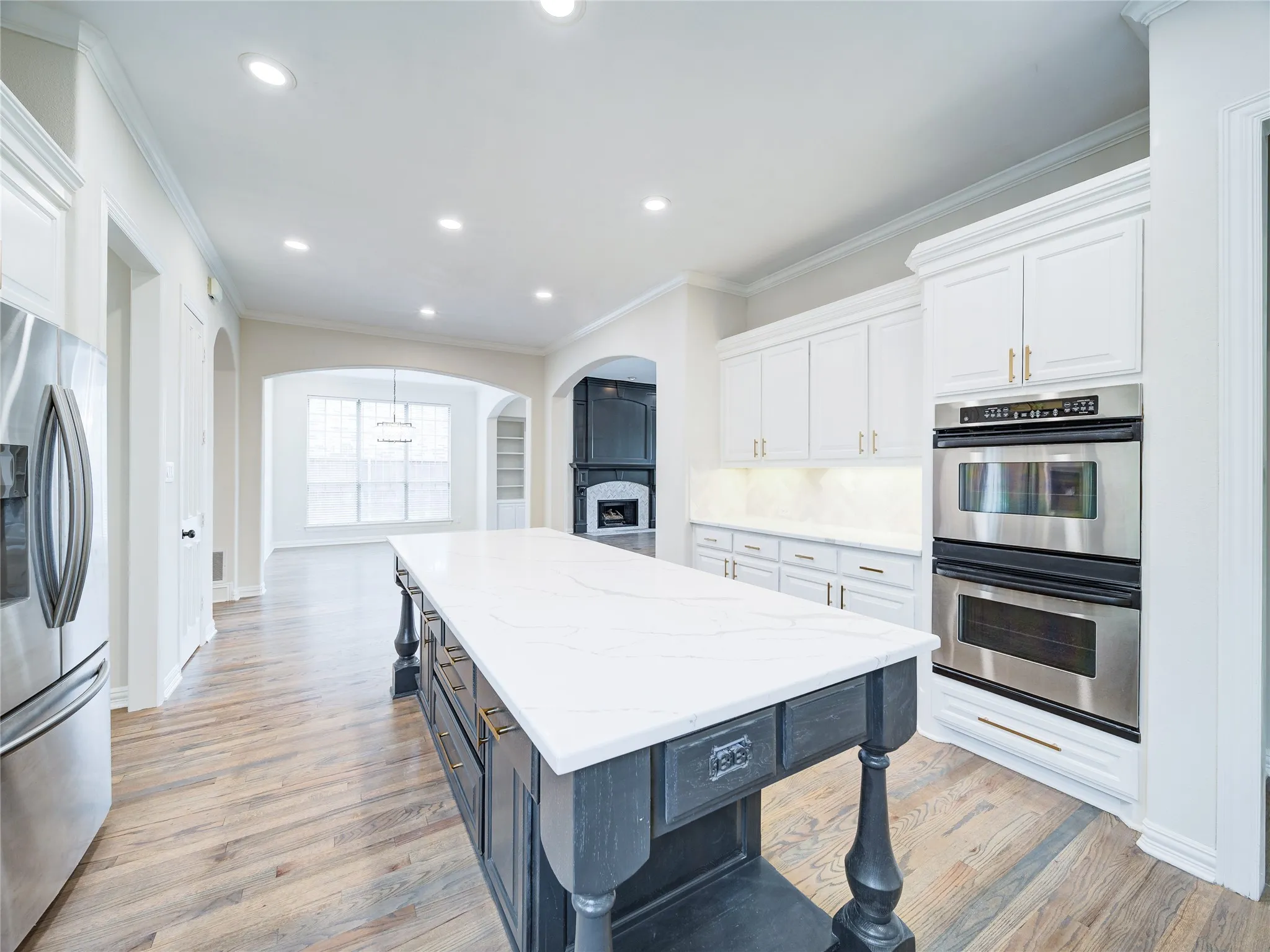 Gourmet kitchen featuring a substantial island with a white countertop, stainless steel appliances, abundant white cabinetry, recessed lighting, and wood-finish flooring