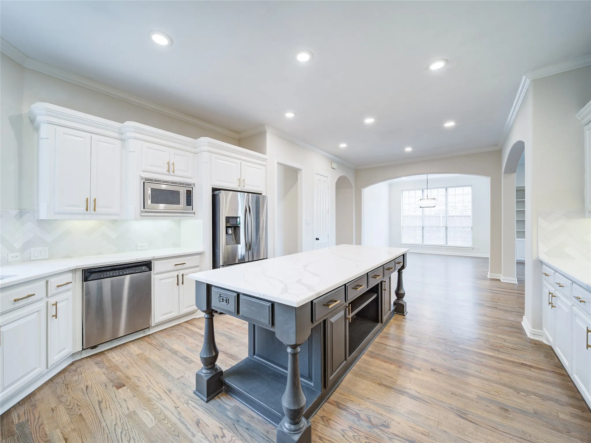 Gourmet kitchen featuring a large central island with seating, stainless steel appliances, white cabinetry with gold-toned hardware, white countertops, and wood-finish flooring